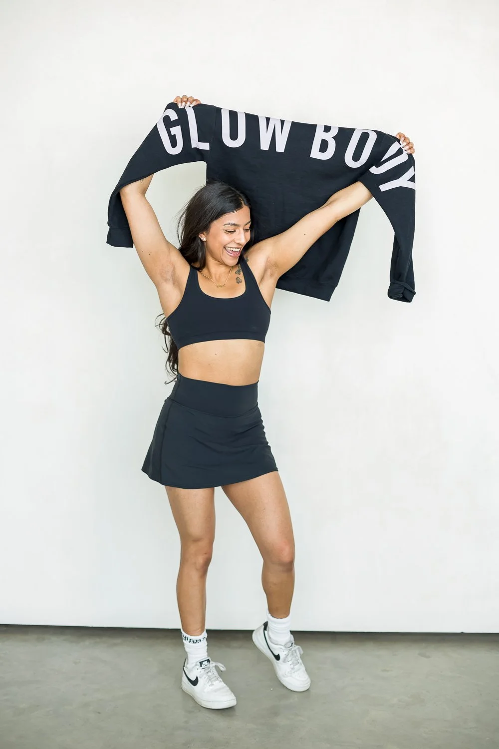 woman holding a branded hoodie, smiling and looking down in fitness clothes