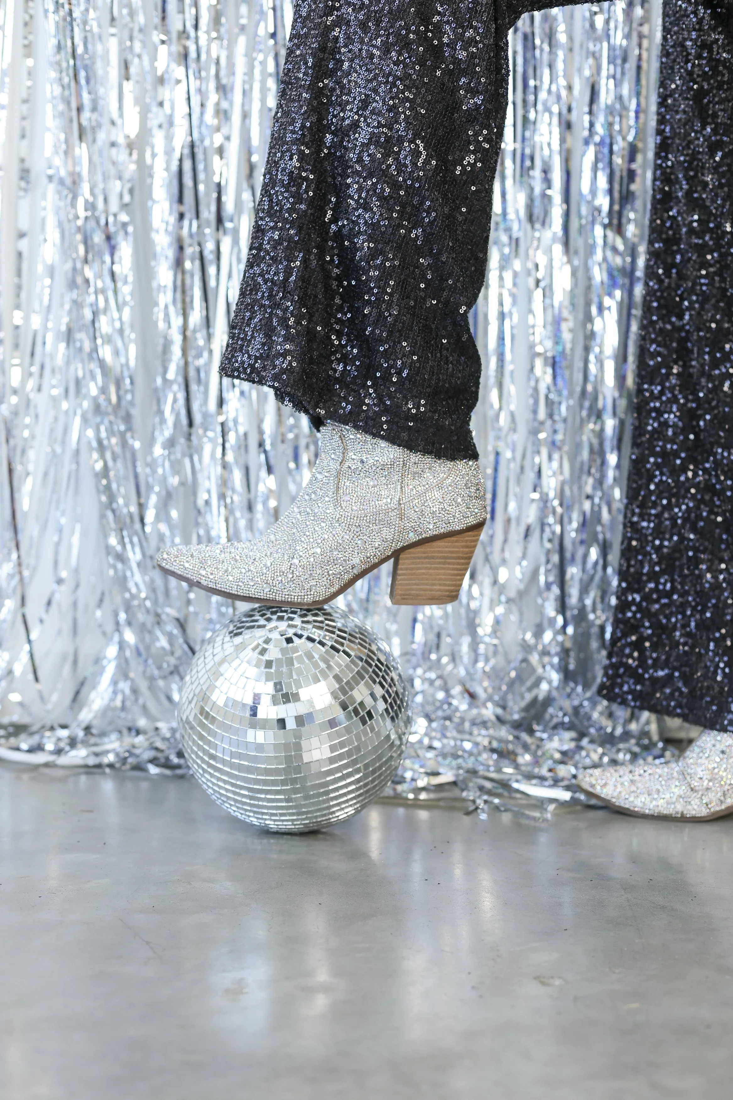 woman's spakly boot stepping on a disco ball with glitter backgrouns