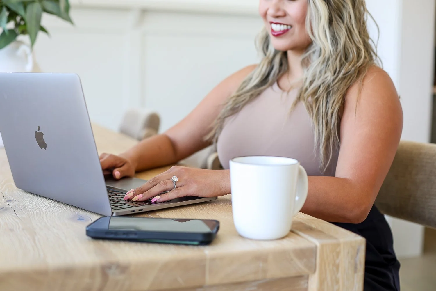 calgary realtor working on computer with phone and mug beside her at kitchen table