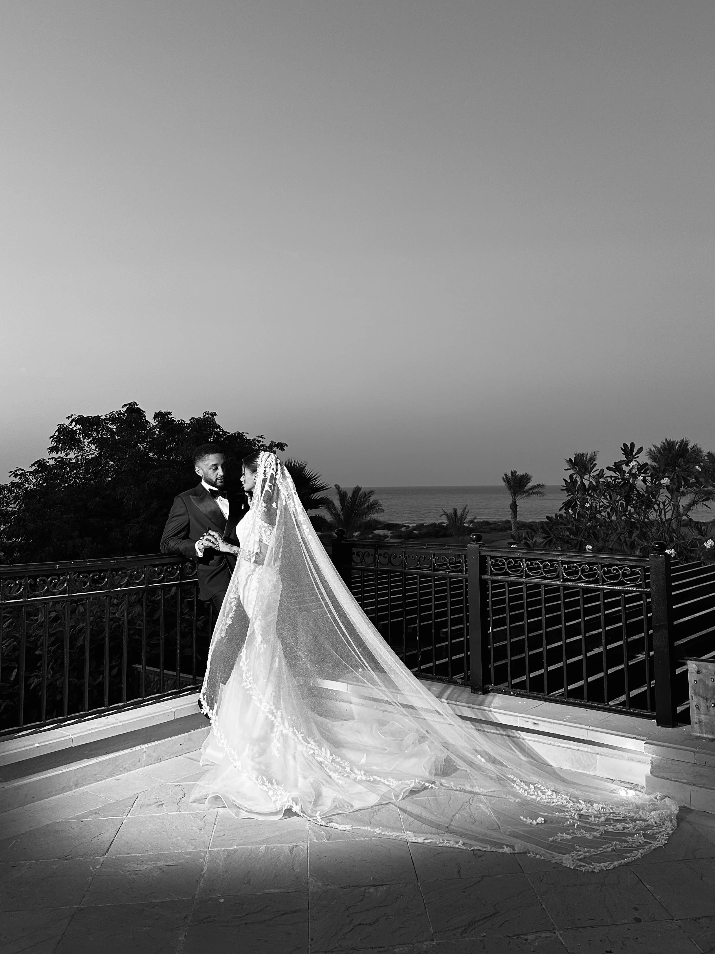 A black and white photo of a bride and groom standing on a balcony, wedding content creator dubai, wedding content UAE, wedding photography and videography, best wedding content creator dubai, wedding content creation expat