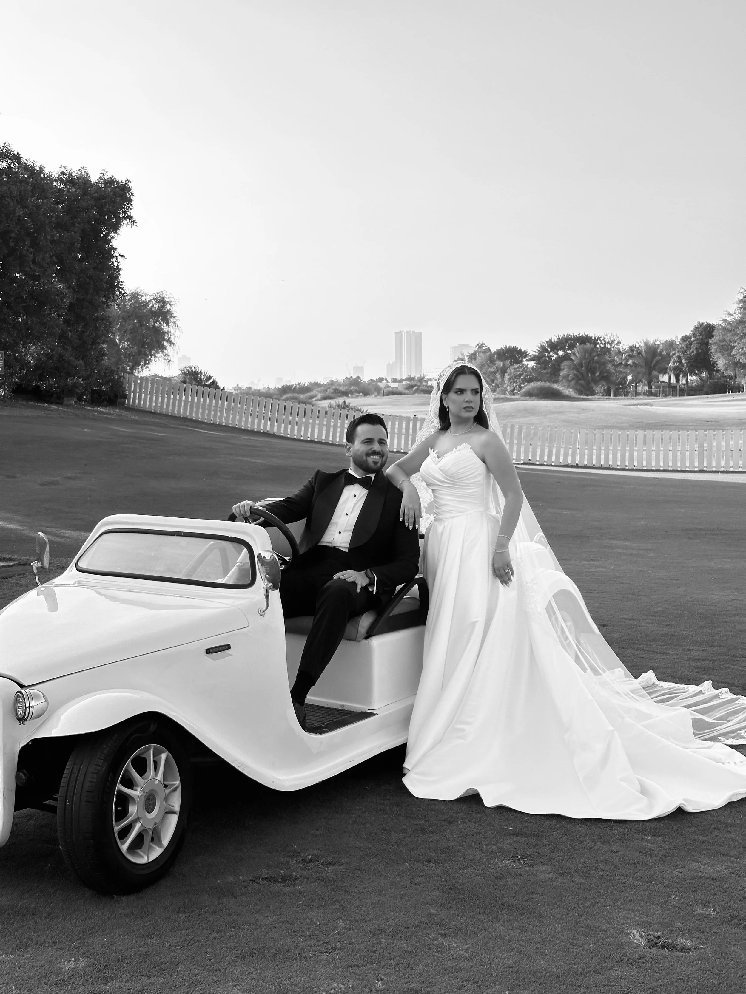 Black-and-white photo of a bride in a white wedding gown and a groom in a tuxedo on a golf cart in dubai. wedding content creator dubai, wedding content UAE, wedding photography and videography, best wedding content creator dubai, wedding content cre