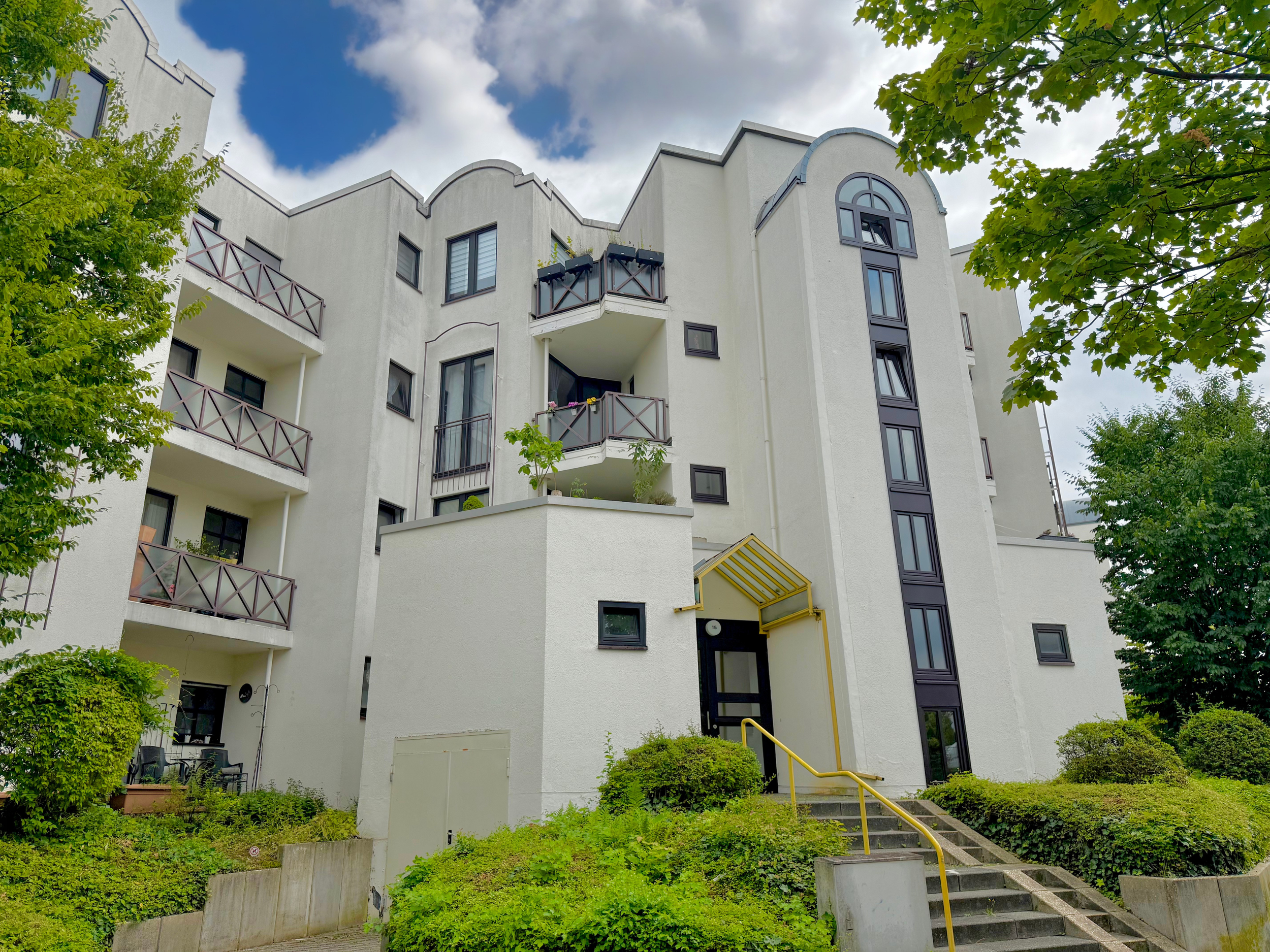 Modernes Wohnzimmer mit großen Fenstern, weißem Sofa, schwarzen Kaffeetisch, Rattan-Kommode, Pflanzen und minimalistische Dekorationen.