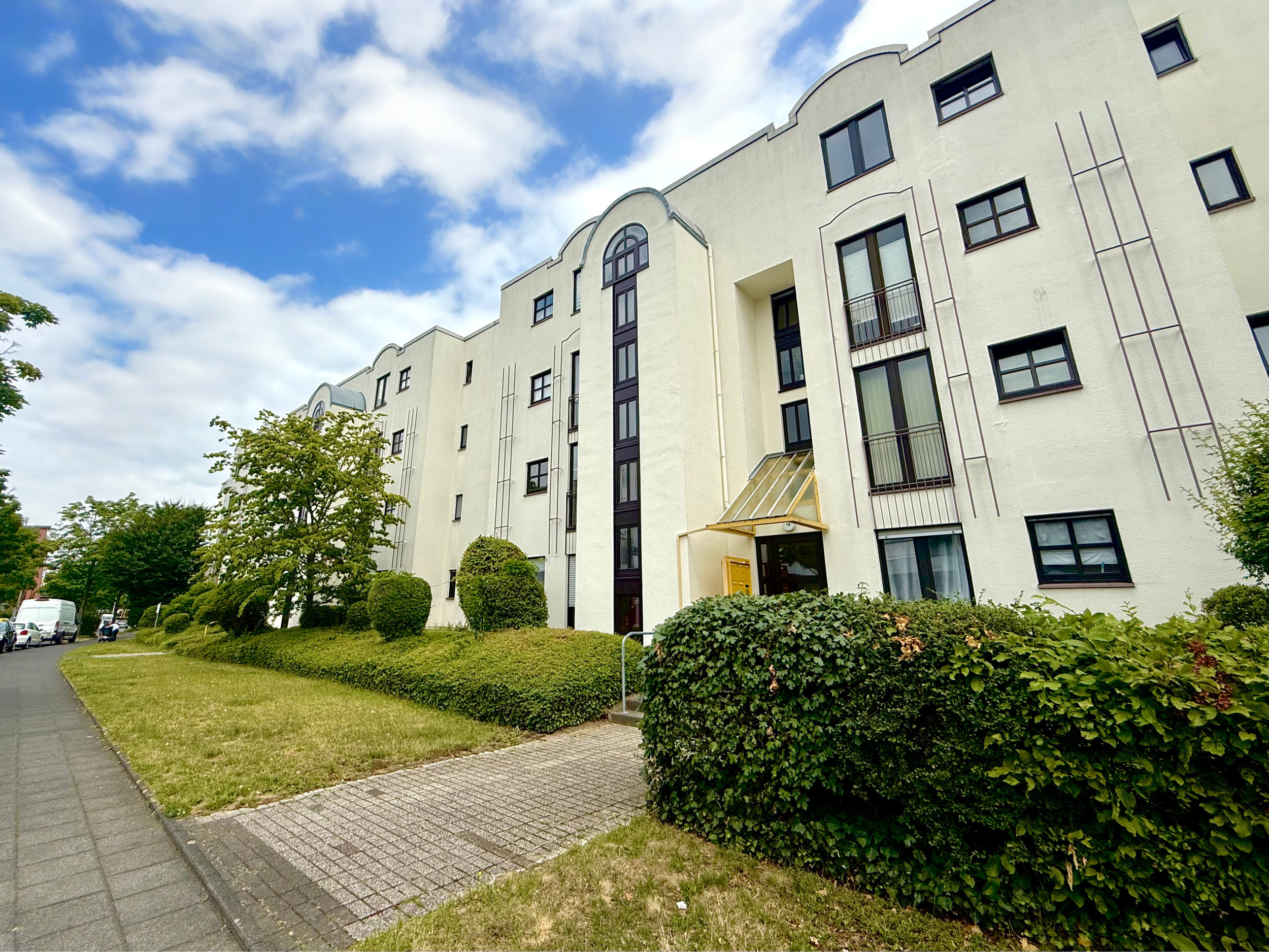 Schlafzimmer mit grünem Bettgestell, vier Kissen, Nachttischen mit Dekorationsgegenständen, Wandbild mit Blattform, weißem Kleiderschrank, Holzfußboden und Heizkörper.