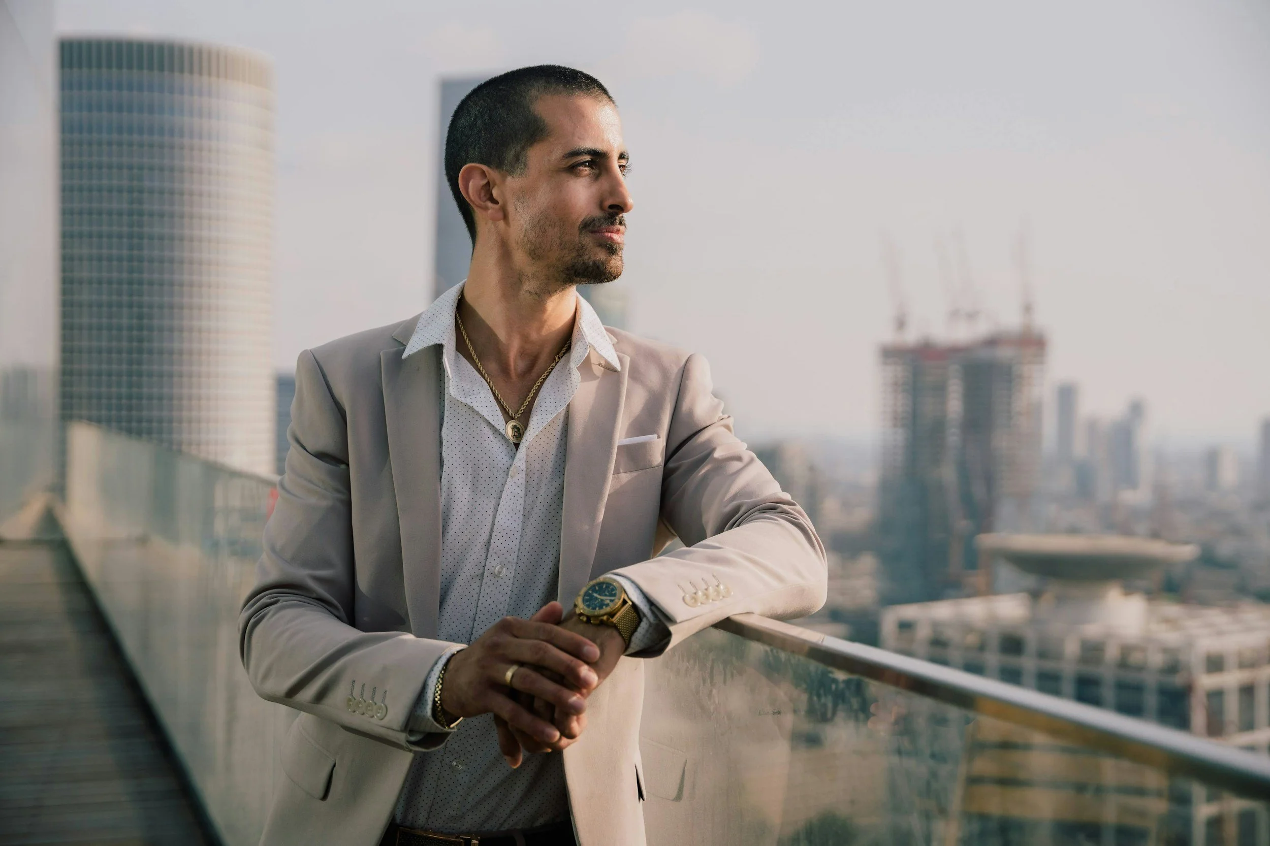 Smartly dressed man in a tan suit looks out across the city in front of him