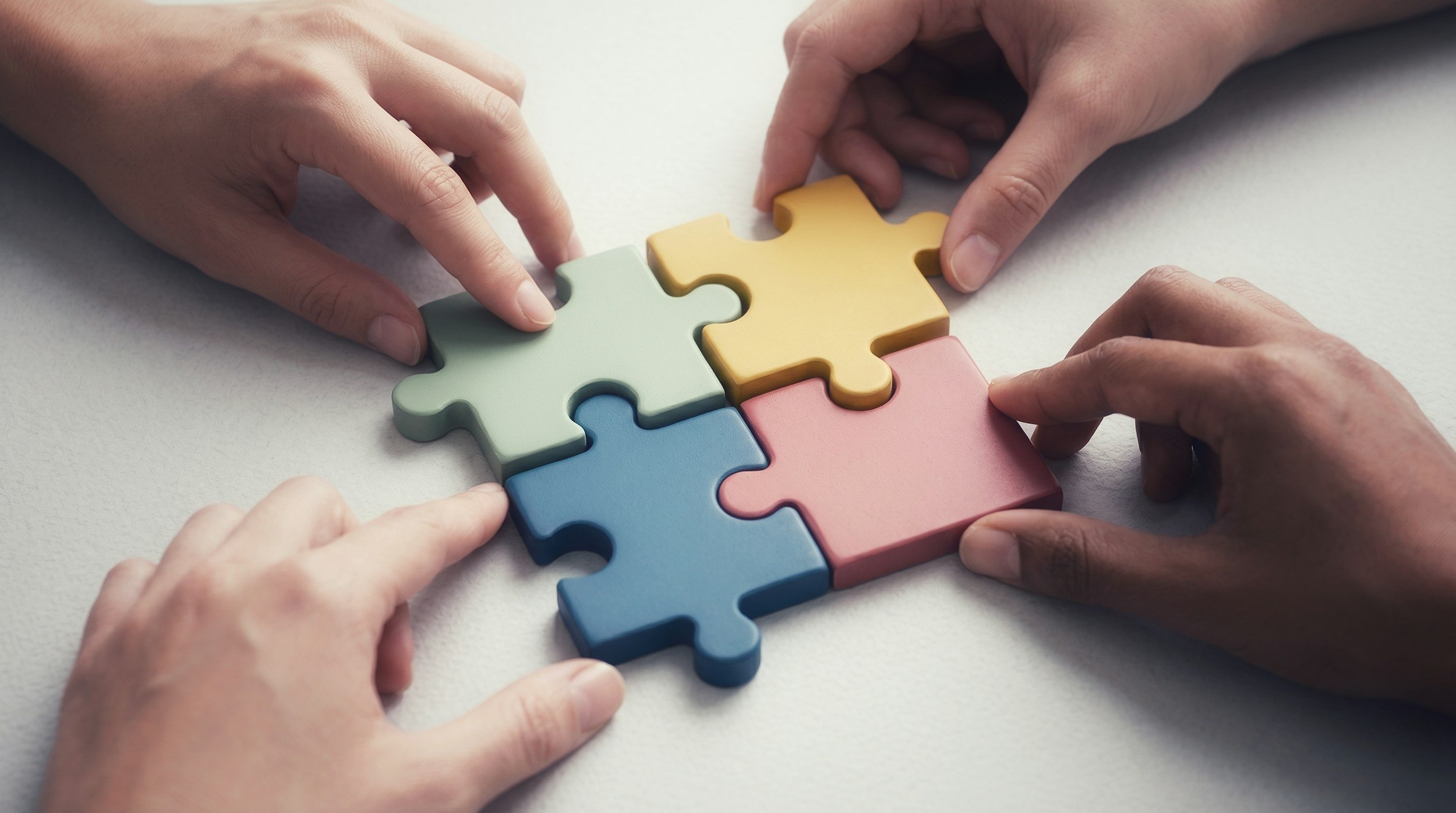 Four people applying puzzle pieces to form a larger single puzzle