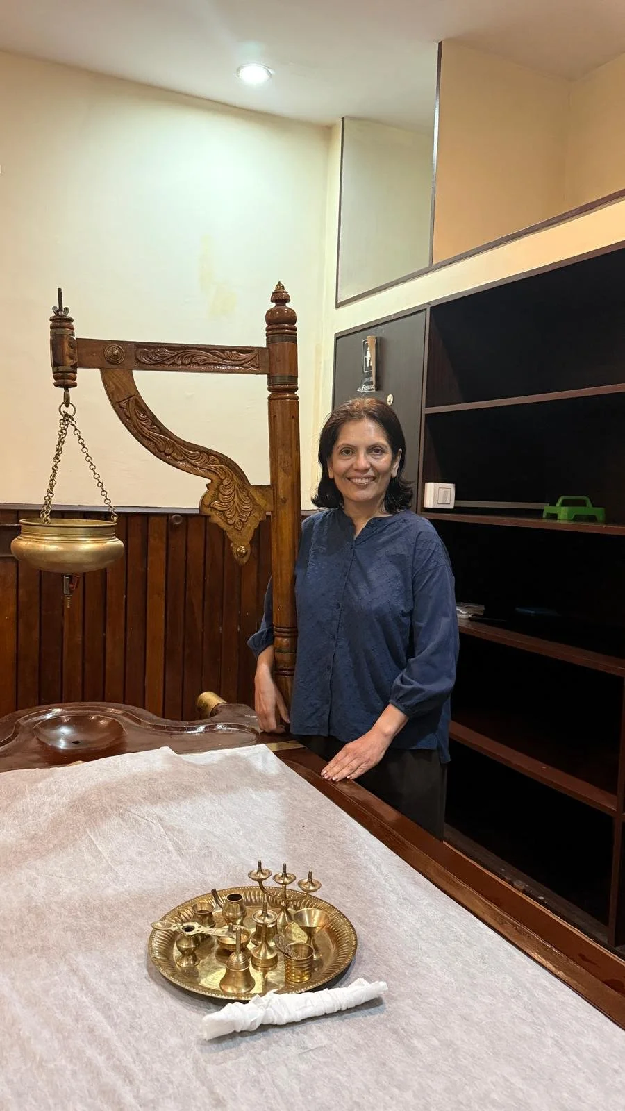 Anu stands beside a wooden massage table with oil suspended above it