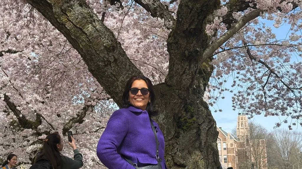 Anu stands in front of a cherry blossom tree on University of Washington campus