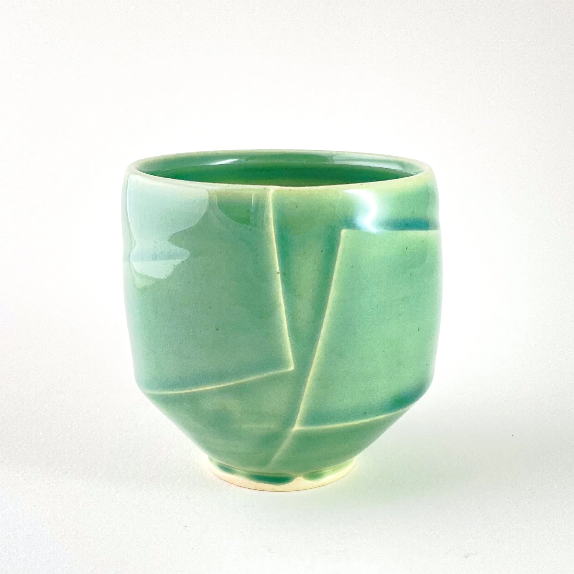 Green ceramic cup with geometric carved design on a white surface against white background