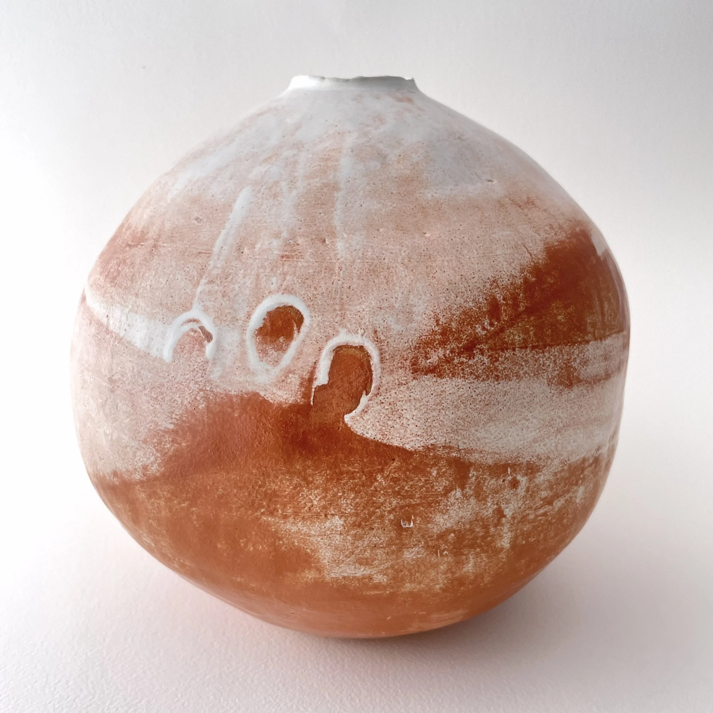 A round, white and tan ceramic vase with a textured surface.
