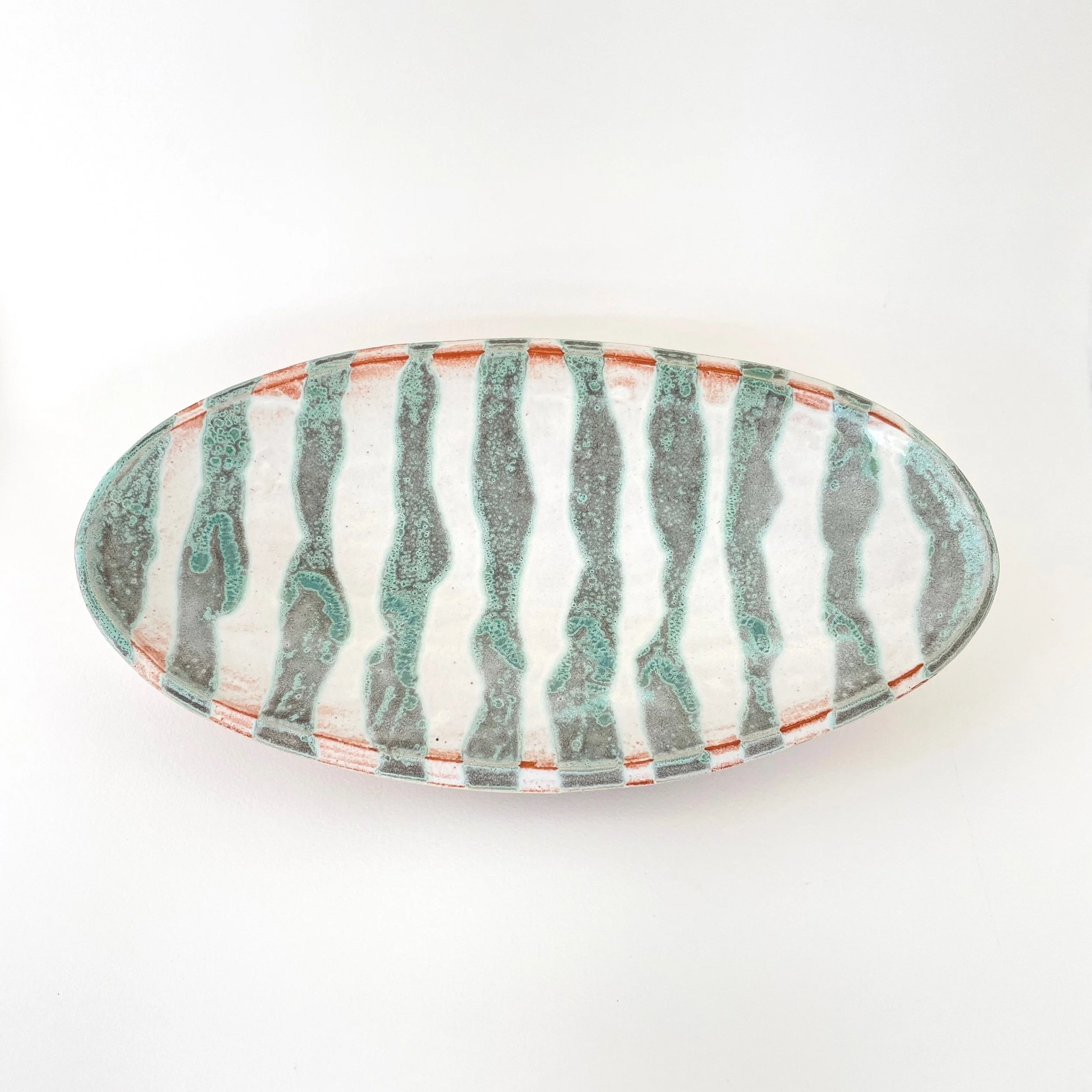 Decorative oval ceramic platter with a striped pattern in green and white on a white background.