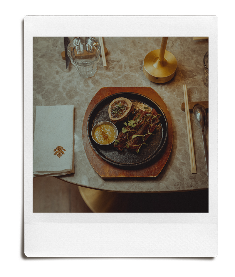 Plate with two halved baked potatoes topped with herbs, small bowl of dipping sauce, and a serving of salad with greens and microgreens, set on a round wooden tray