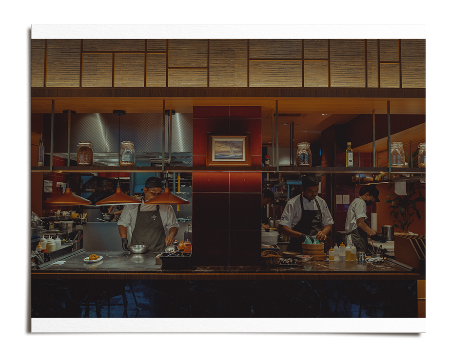 Chefs preparing food in a modern restaurant kitchen with a red and wood interior.