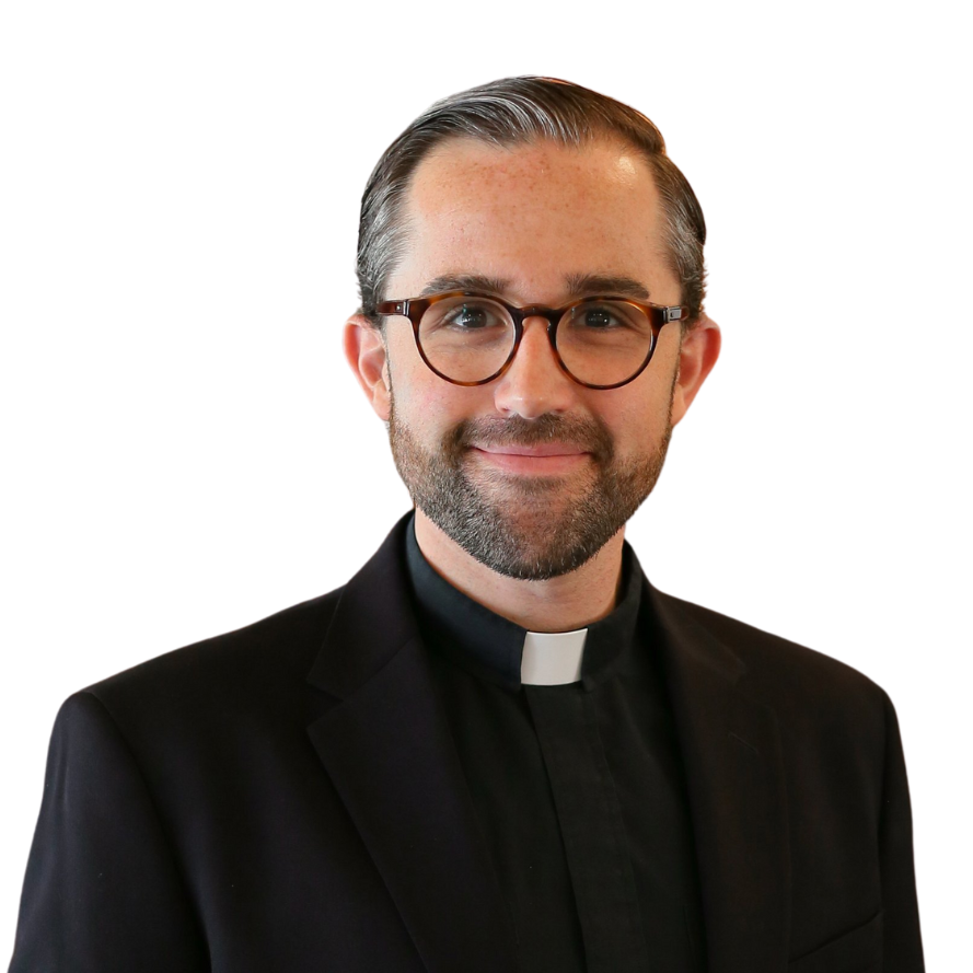 A smiling man dressed as a priest with glasses, a beard, and wearing a black clerical shirt with a white clerical collar.