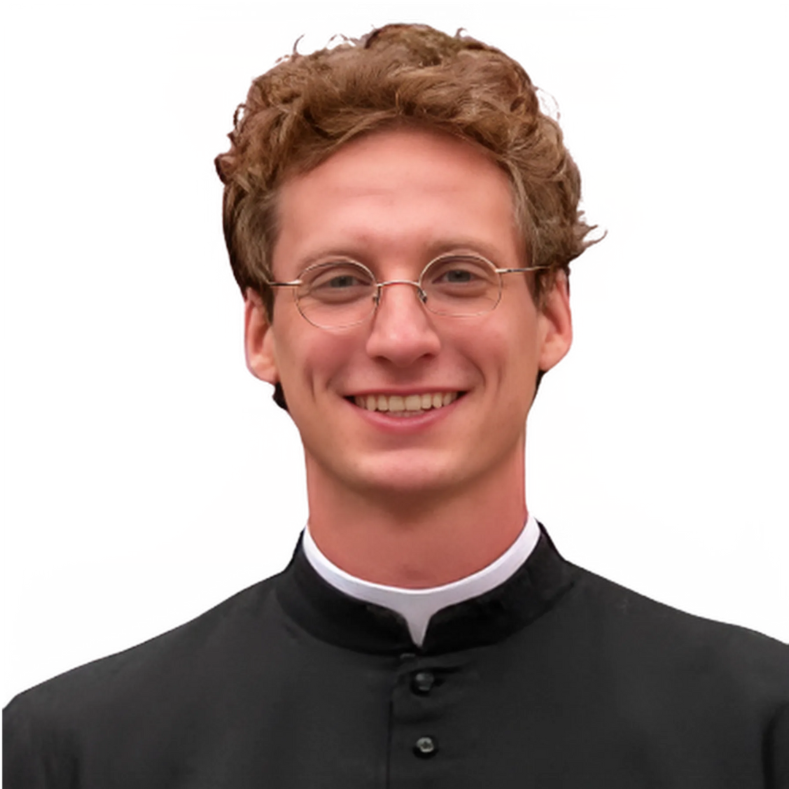 Young man with glasses, smiling, wearing a black clerical shirt with a white collar, standing in front of a red and yellow background.