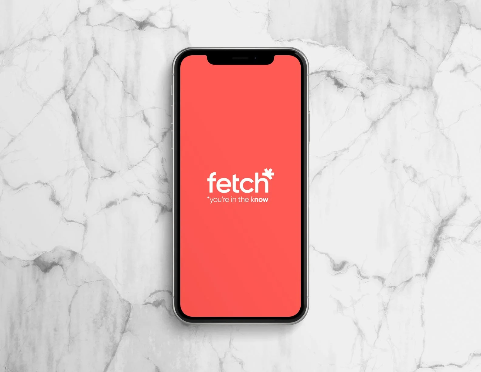 An iPhone displaying the Fetch app logo on a red background, placed on a white marble surface.