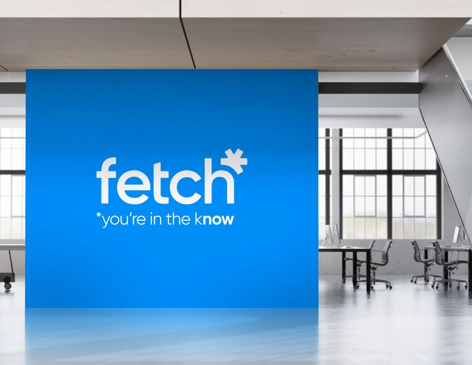 A modern office space with large windows, a wooden ceiling, and a blue wall with the Fetch logo and the tagline '*you're in the know'.
