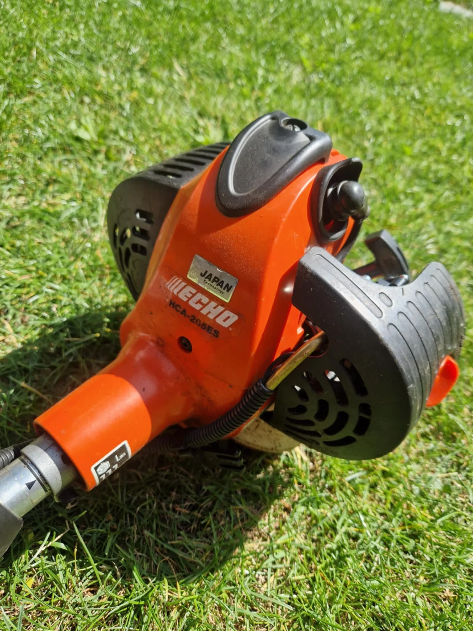 Close-up of an orange Echo gas-powered hedge trimmer with black handles, lying on green grass.