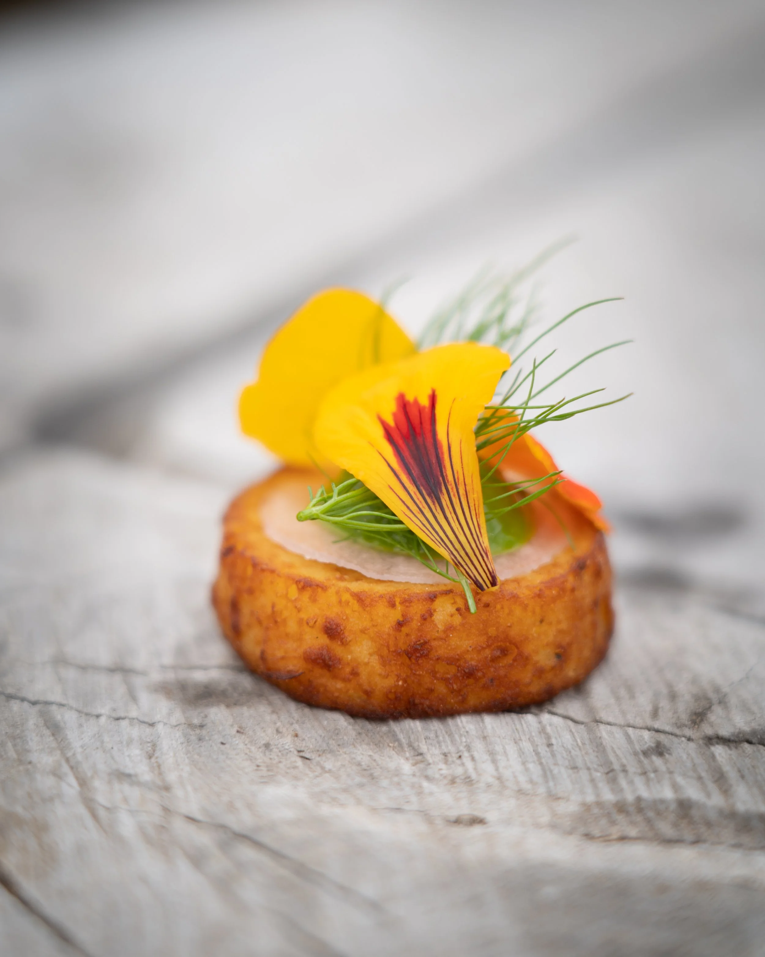 Fried food topped with yellow and orange edible flowers and green herbs on a rustic wooden surface.