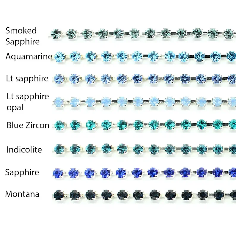 An array of small, round gemstone earrings in various shades of blue, black, and clear, arranged in rows with labels indicating different types of sapphires, aquamarine, topaz, zircon, and indicolite.