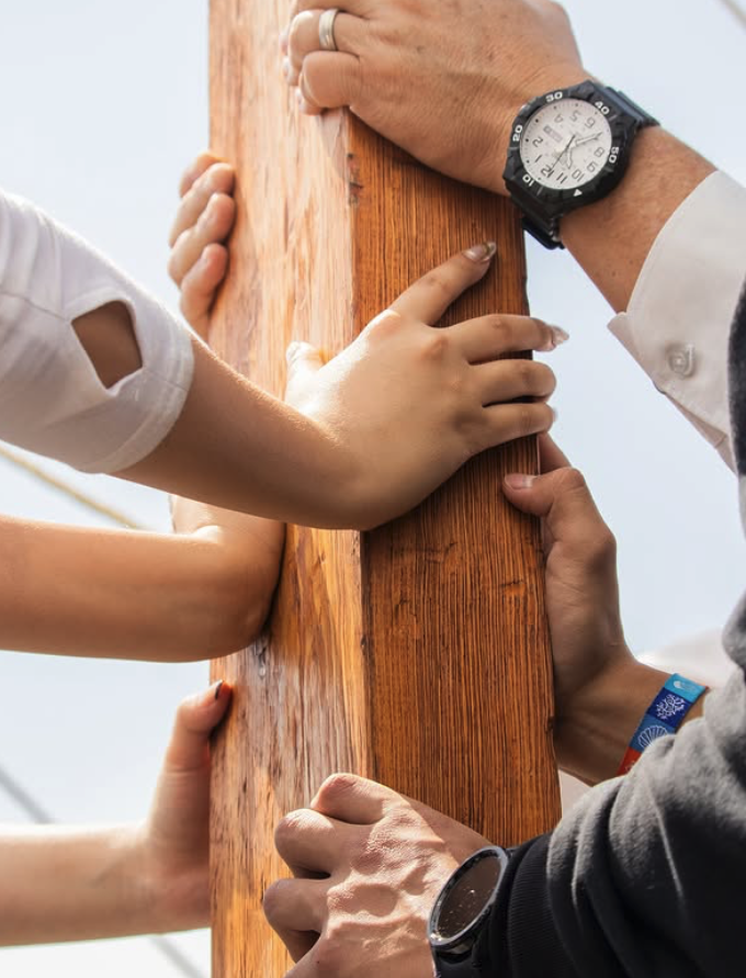 Diversas manos de diferentes personas sosteniendo una cruz de madera en un entorno exterior.
