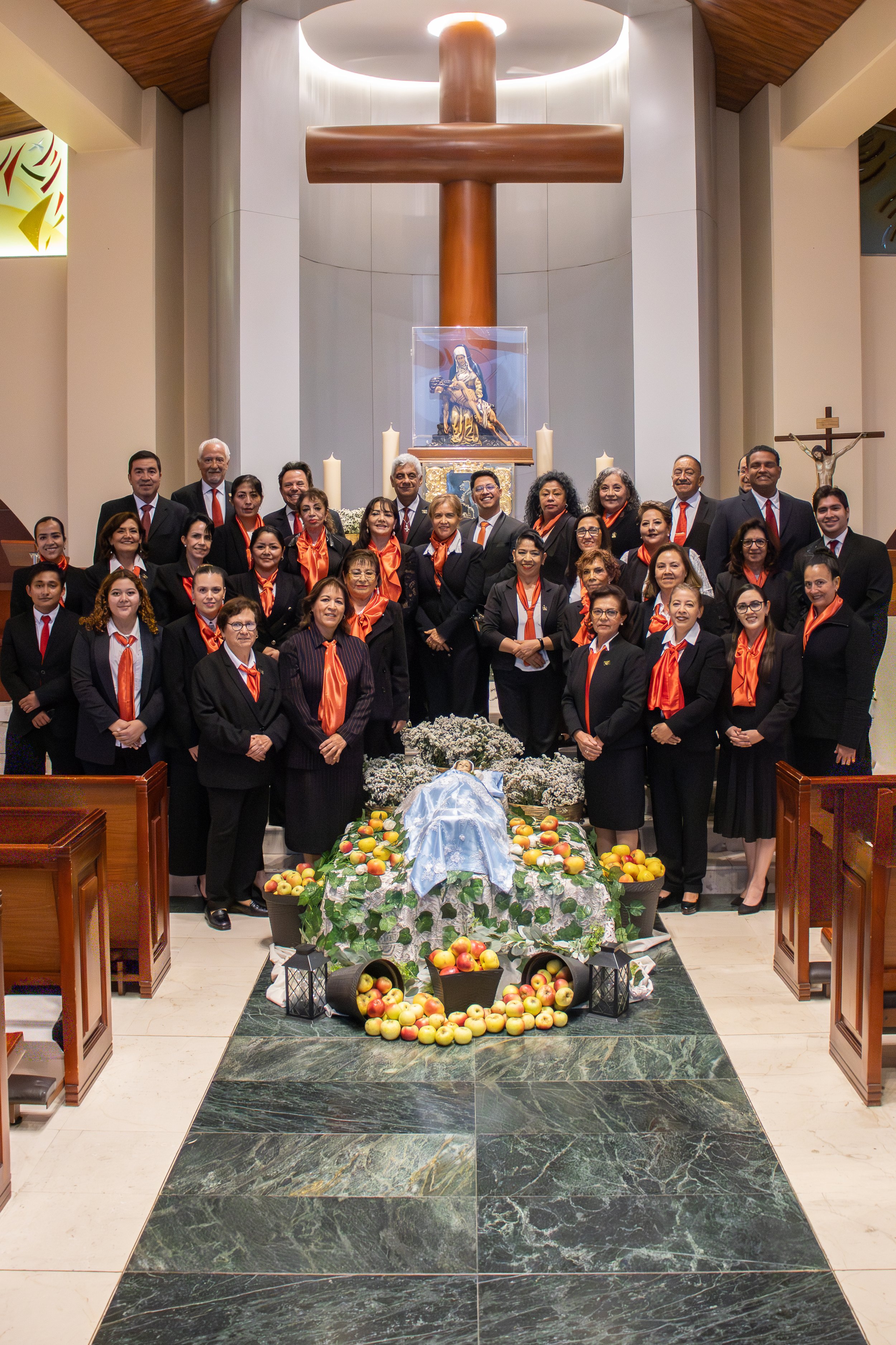 Grupo de personas en una iglesia, participando en un evento religioso con una figura de la Virgen en un altar decorado con flores, fruta y velas.