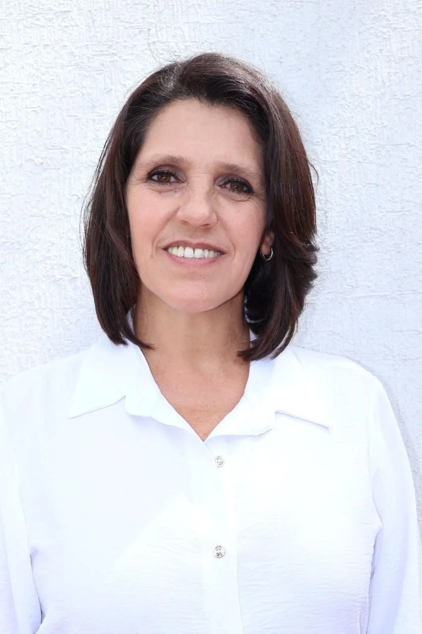 Mujer sonriendo, de cabello castaño oscuro, vestido blanco, fondo blanco. Kathia Orozco Lozano.