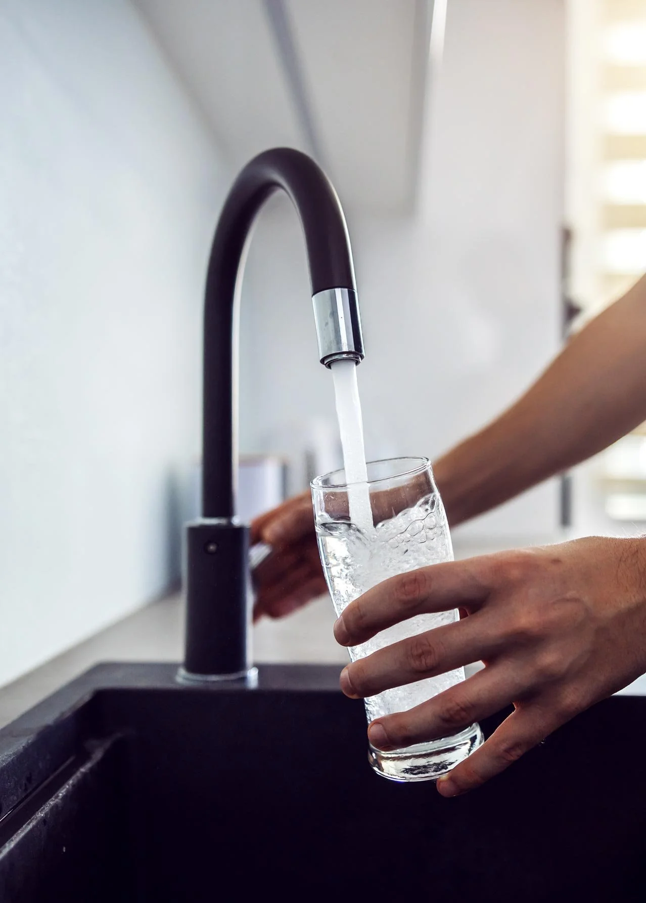 A man filling a glass with water from the kitchen sink
