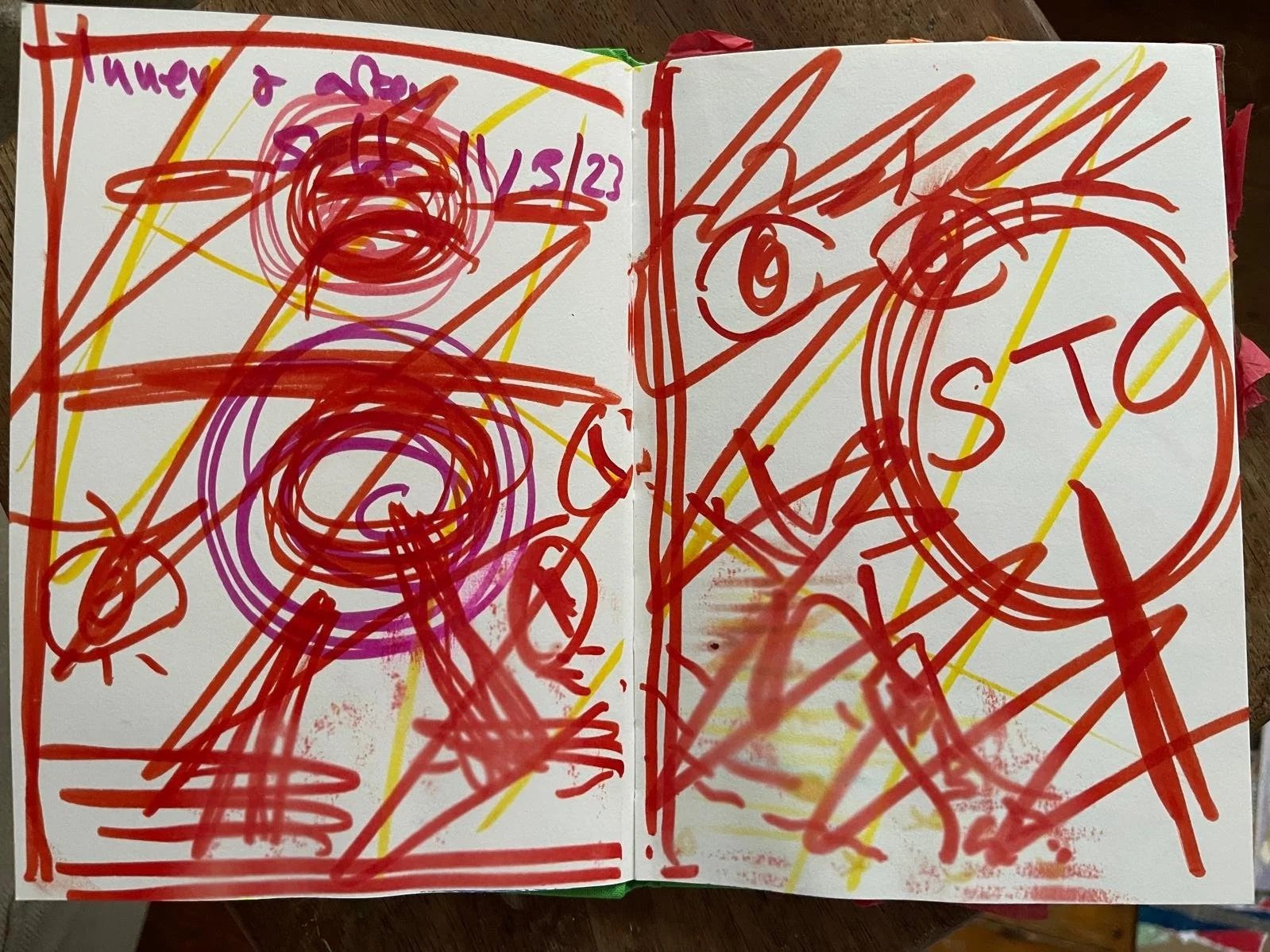 Colorful, chaotic childlike drawing on a white paper with red, yellow, purple, and pink markers. The drawing features circles, lines, scribbles, and words such as 'SOT' and 'WE'.
