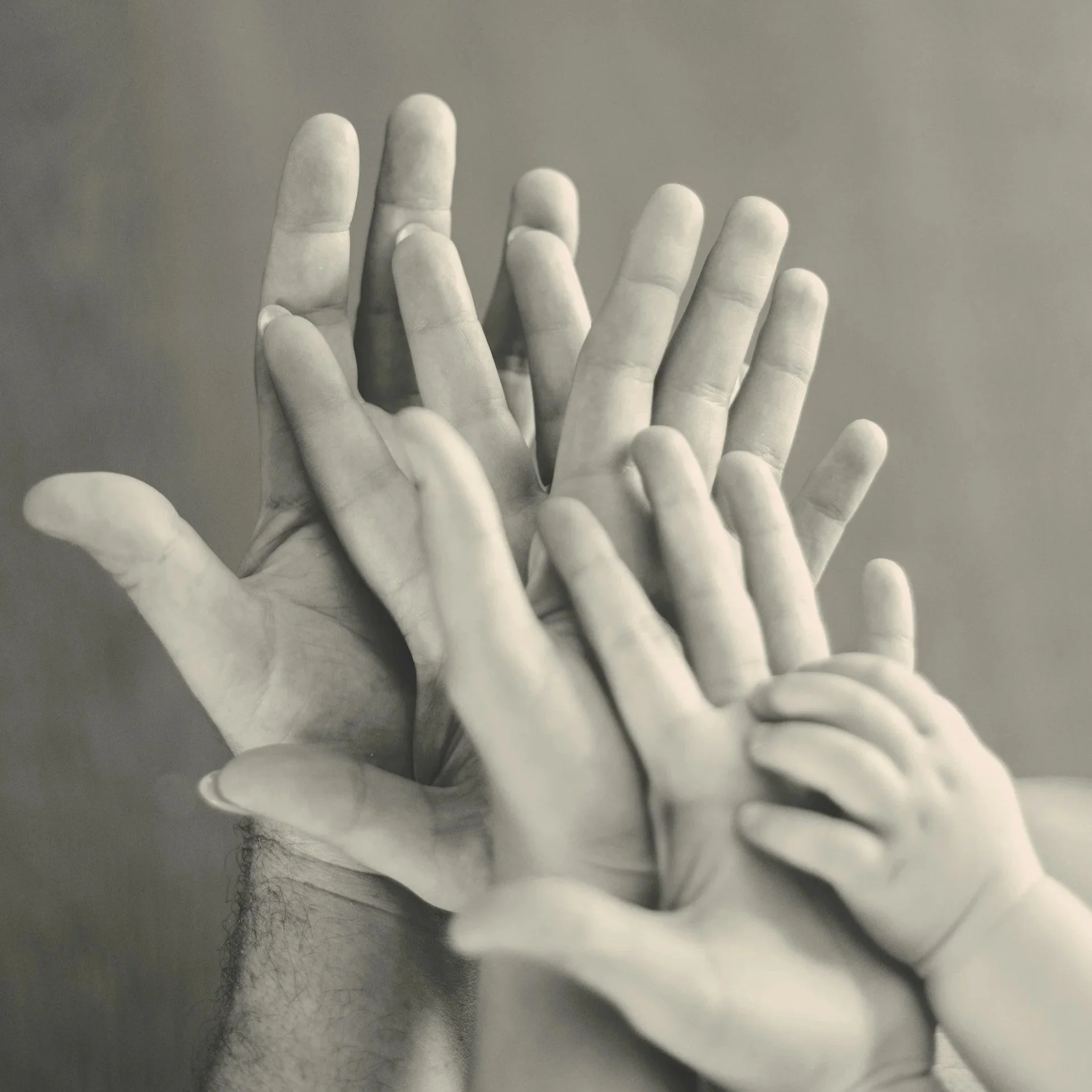 Monochrome close-up photo of multiple hands, including a child's hand, stacked together with palms open.