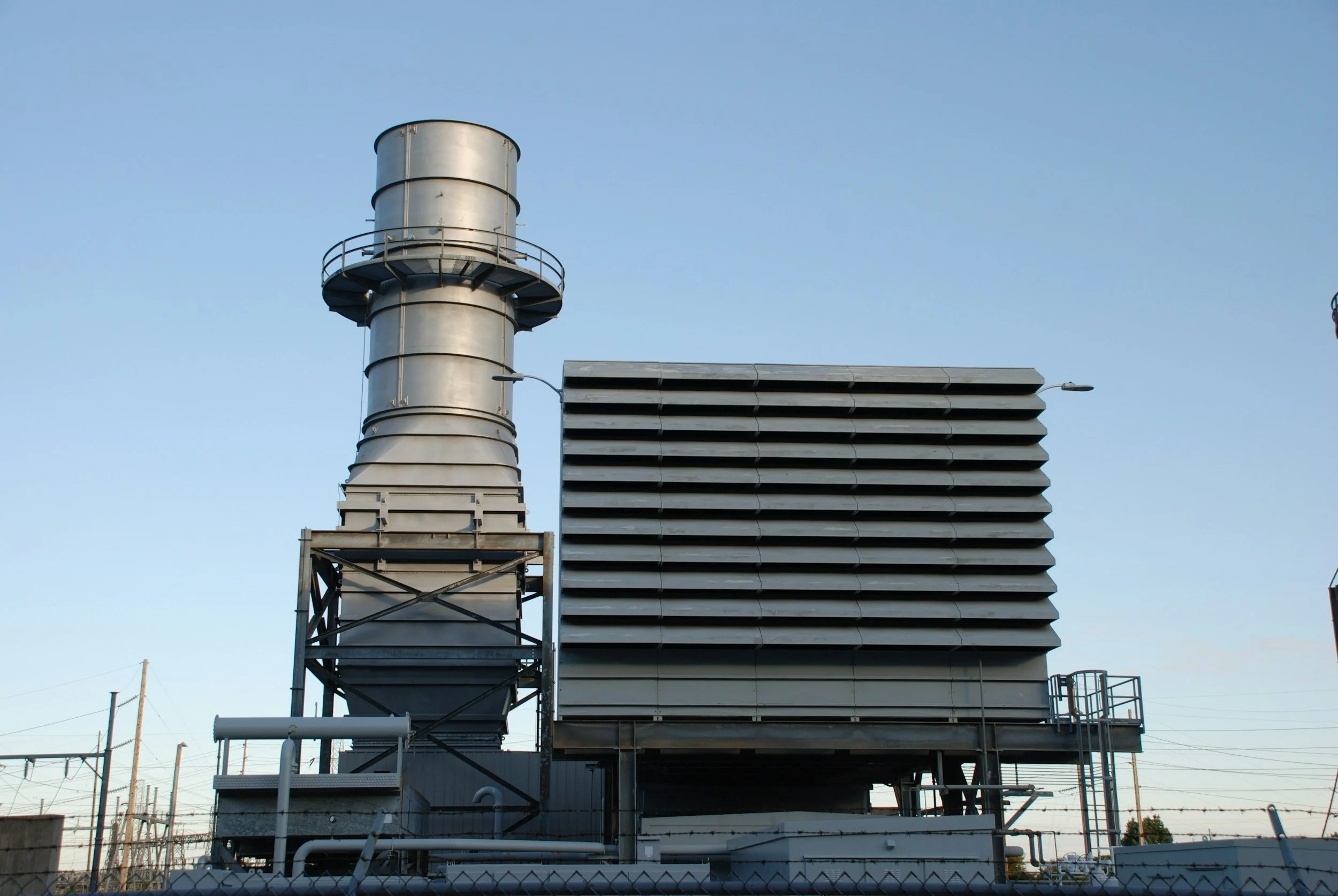 Industrial building with large ventilation system and exhaust stack against a clear blue sky.