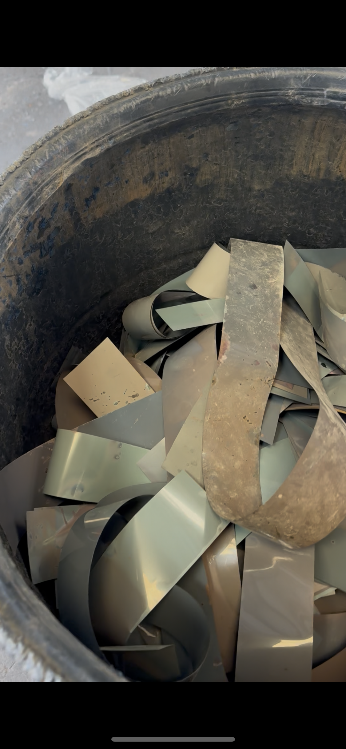 A close-up of a metal scrap container filled with curled and bent strips of shiny metal, with rusted and dirty edges.