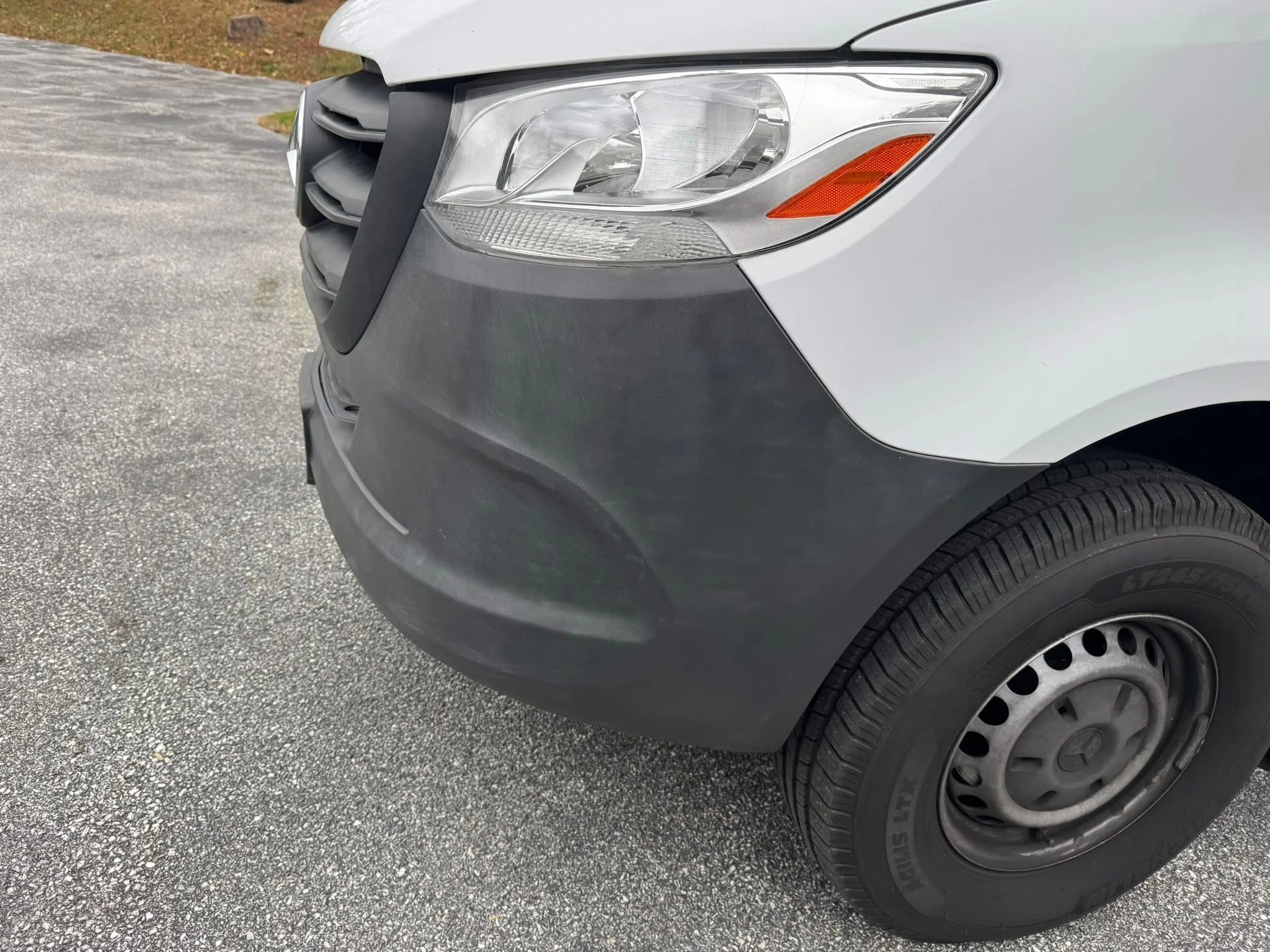 Front right side of a silver van with black bumper and tire, parked on a gravel surface.