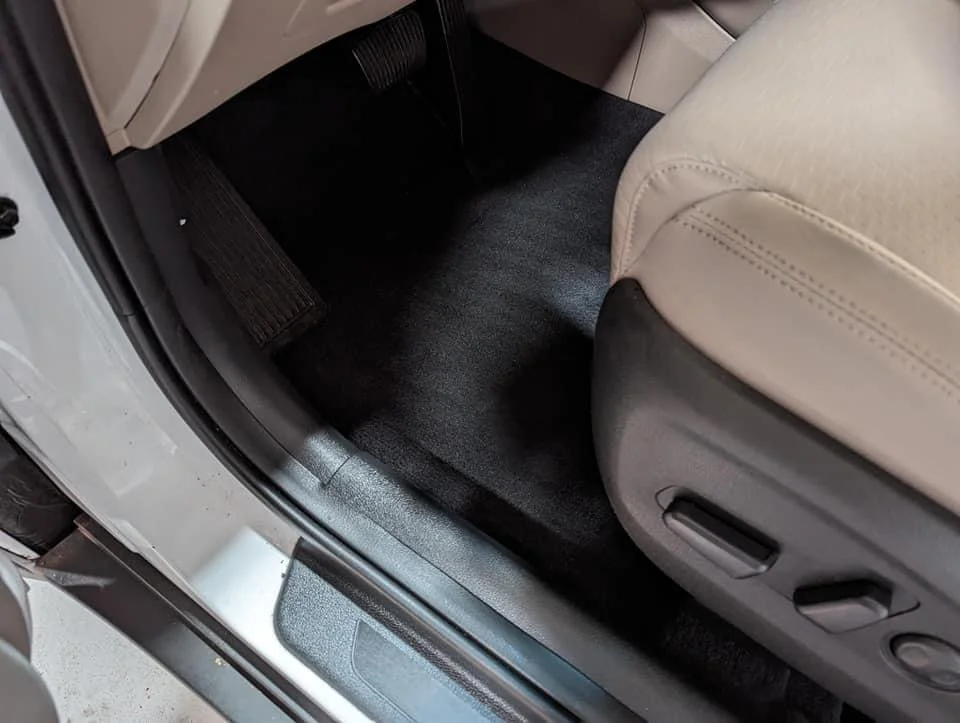 View of the interior car floor area showing beige seat, black carpet, and door sill.