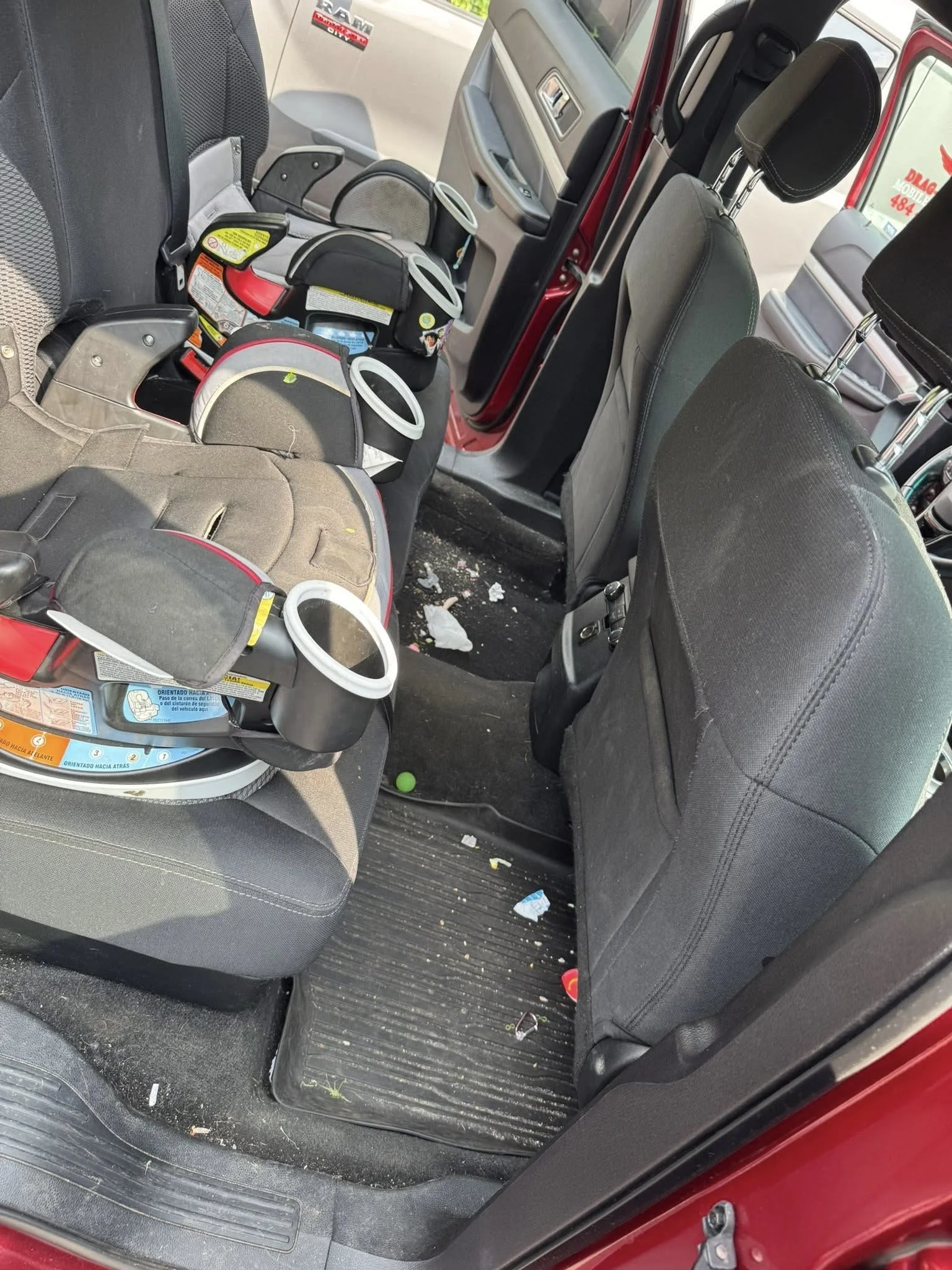 Backseat of a vehicle with a child car seat, some trash, and debris on the floor and seats.