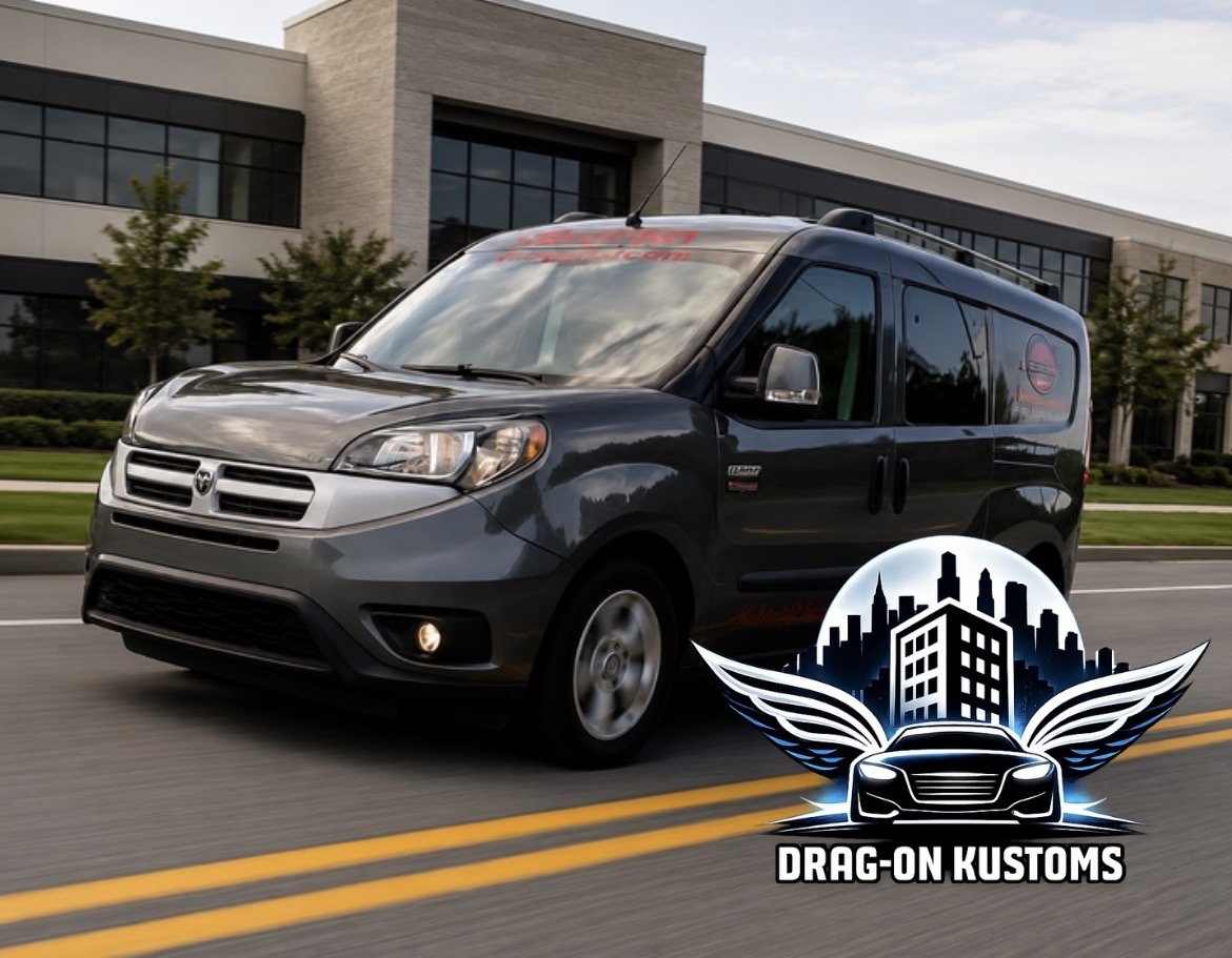 A black Dodge Caravan driving on a city street with a modern building and trees in the background. There is a large graphic overlay of a city skyline, a stylized car with wings, and the text "Drag-On Kustoms" in the bottom right corner.