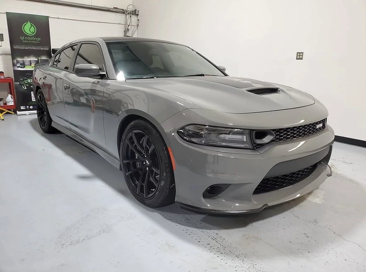 Gray Dodge Charger sedan parked inside a garage with a white wall, black wheels, and a hood scoop.