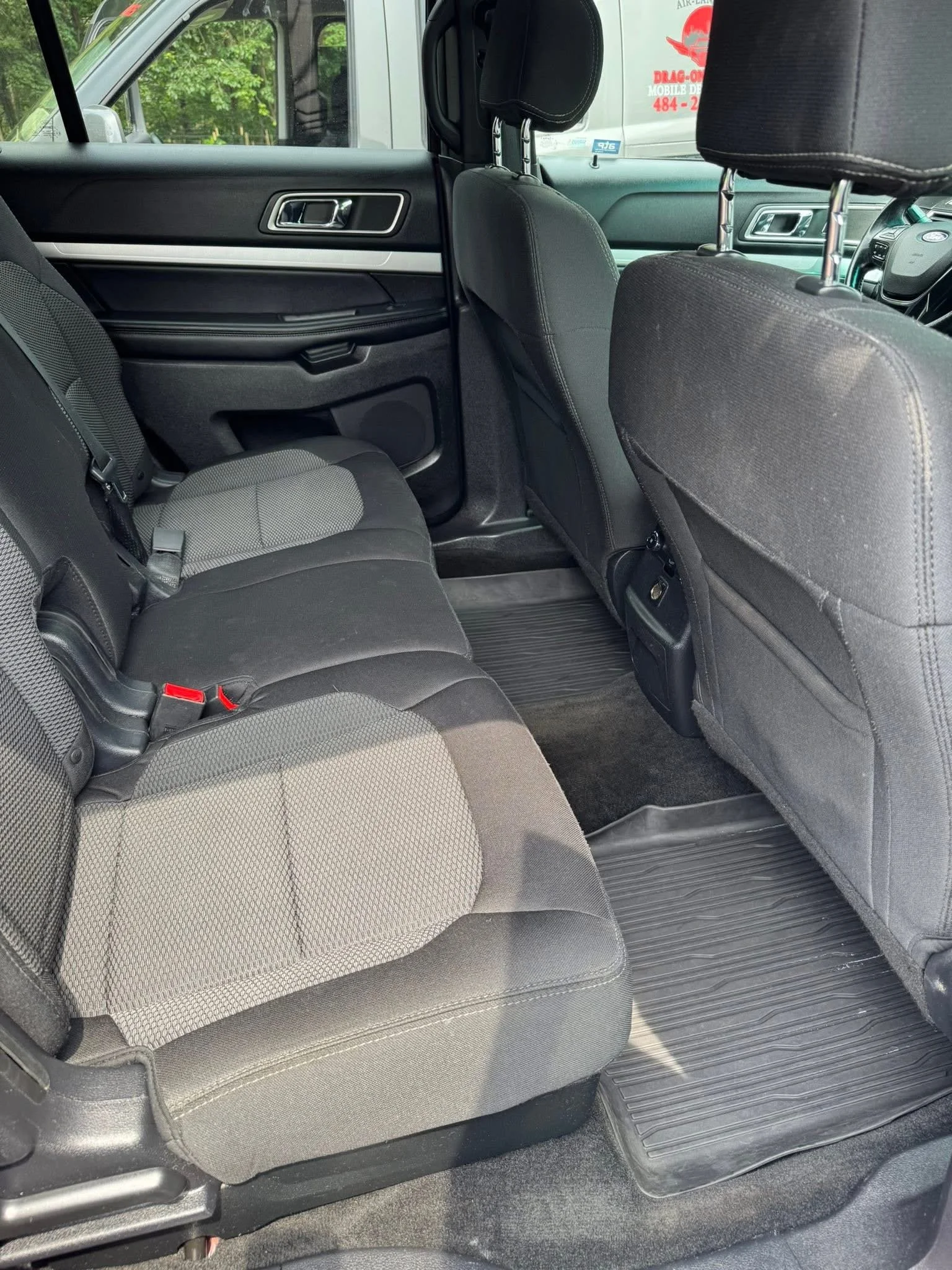 The back seat area of a black pickup truck, showing two rows of fabric seats and a rubber floor mat.