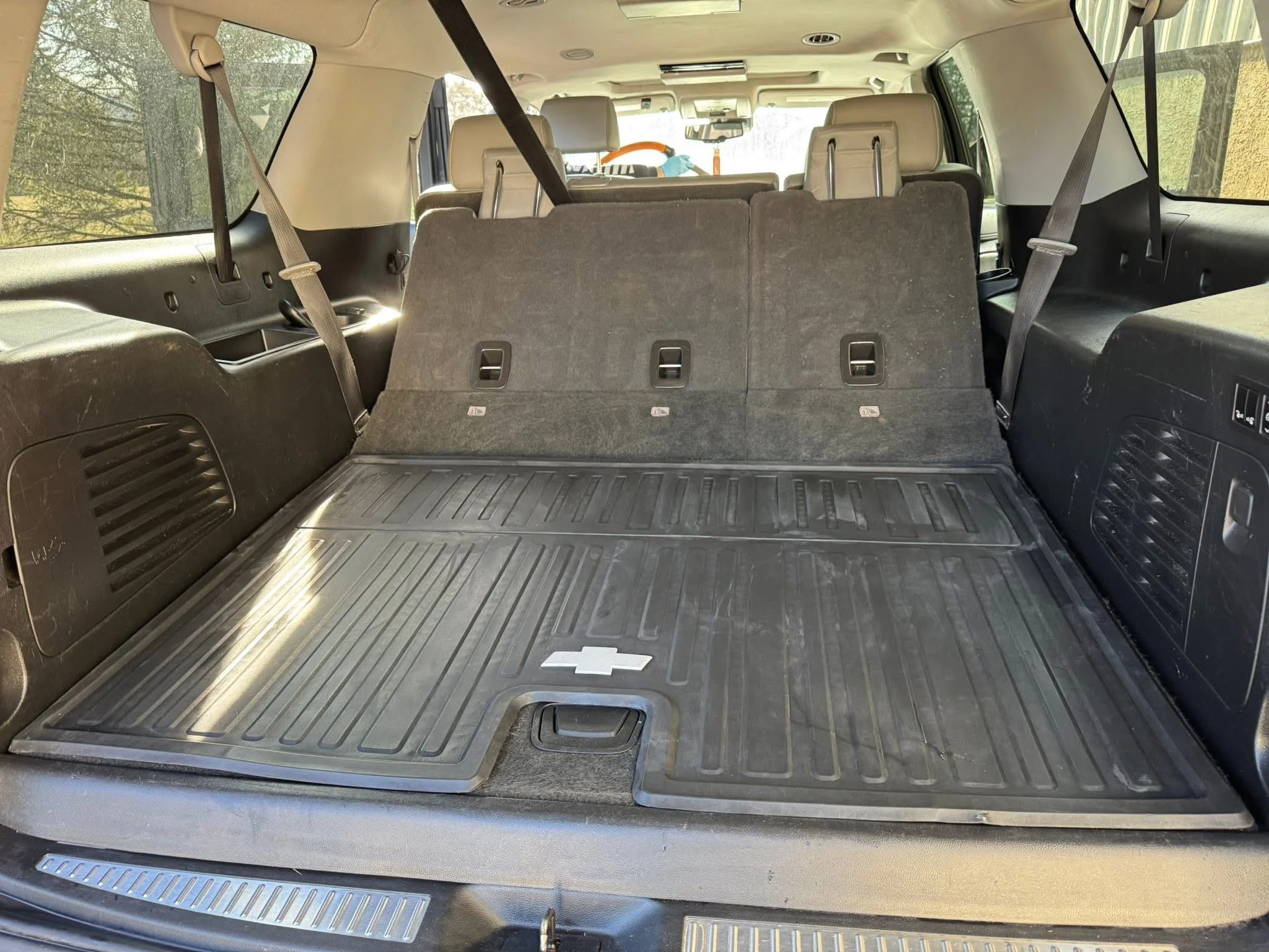 The interior of a Chevrolet SUV viewed from the rear, showing an open cargo area with black rubber flooring and a faint Chevrolet logo, with the back seats and windows visible.
