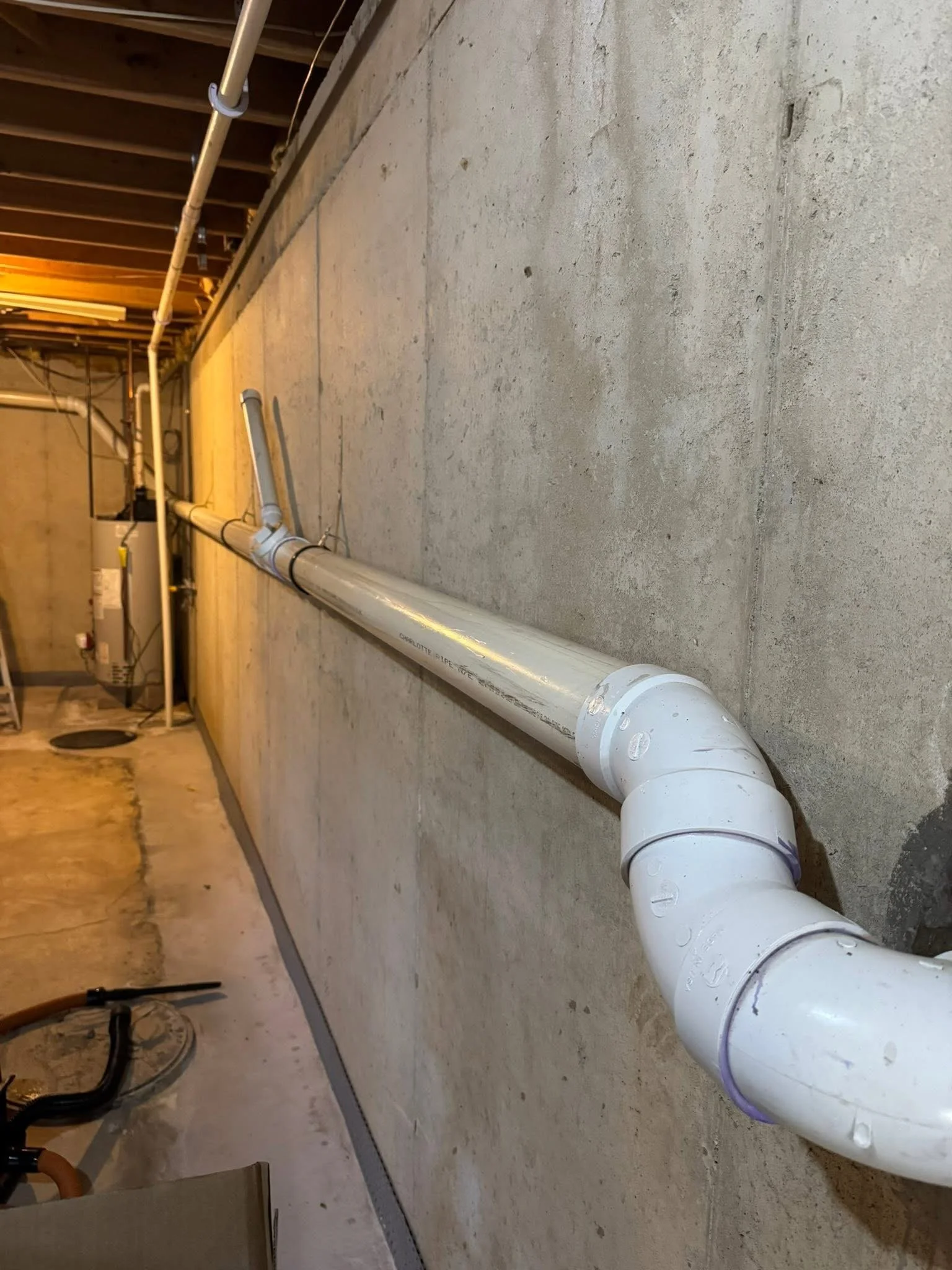 PVC pipes installed along a concrete wall in a basement or utility room.