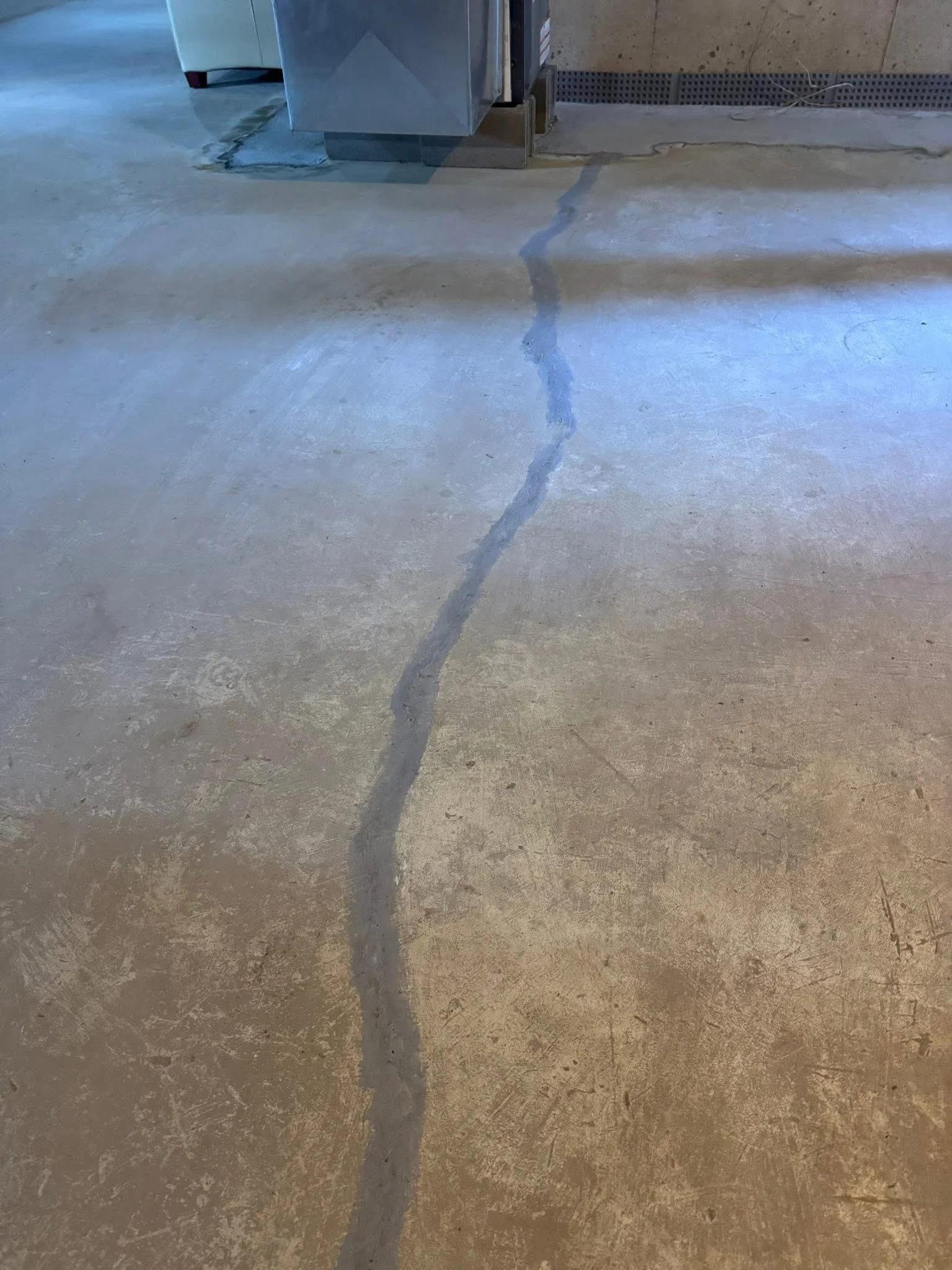 Crack in concrete floor near a wall and a metal vent or electrical box.