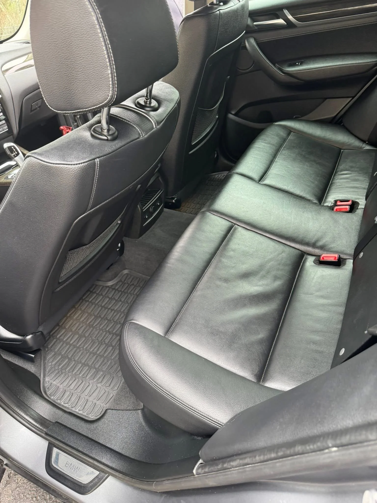 The backseat area of a car with black leather seats, a floor mat, and the front seat backs also visible.