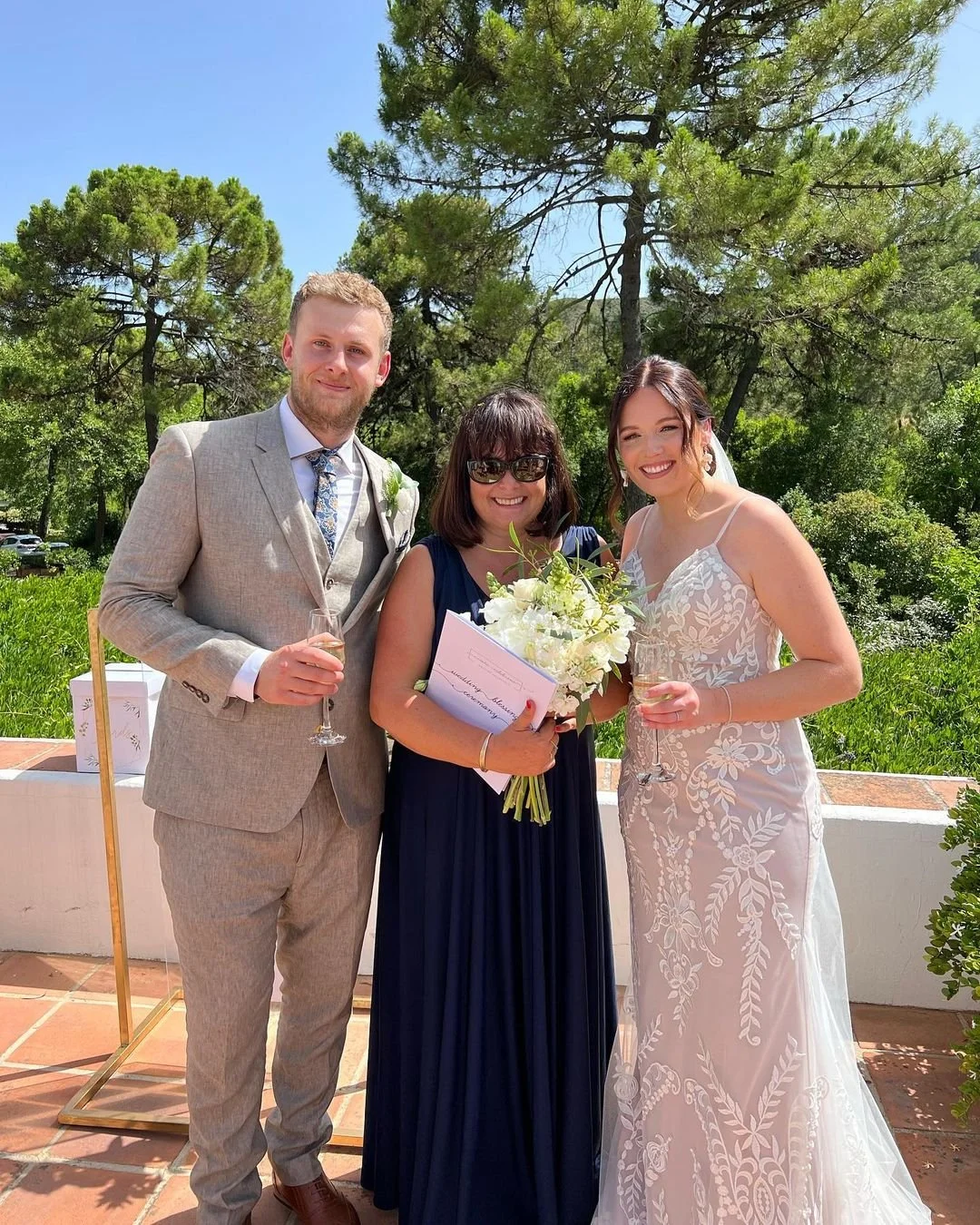 Three people, a man in a light gray suit, Nikki Kulin, professional international Wedding Celebrant who has just delivered their handwritten wedding ceremony in Marbella, Spain.