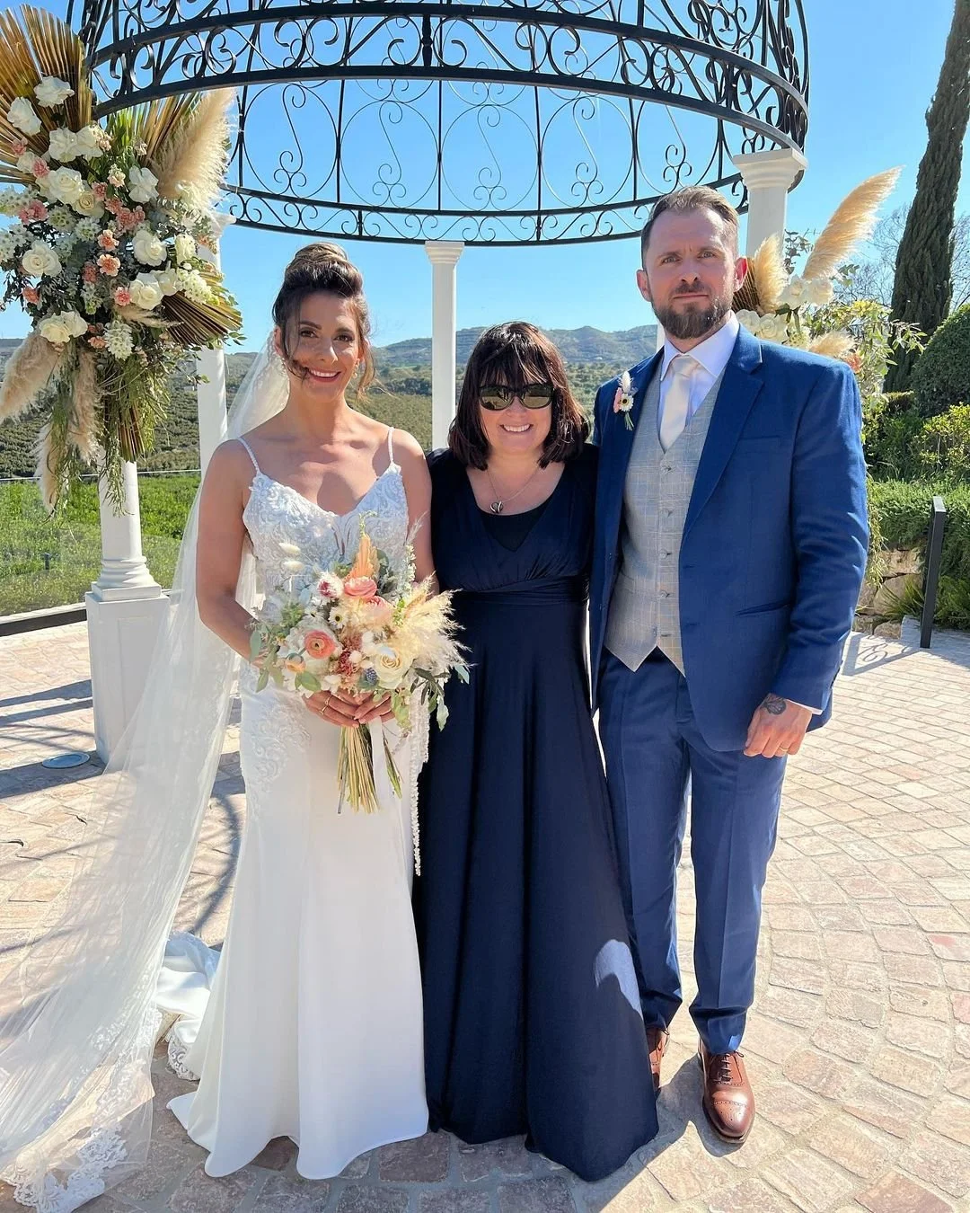 A bride and groom pose with international wedding celebrant, Nikki Kulin, at the ceremony space of the Cortijo Bravo Hotel, Velez Malaga having delivered their handwritten wedding ceremony which included their daughter.