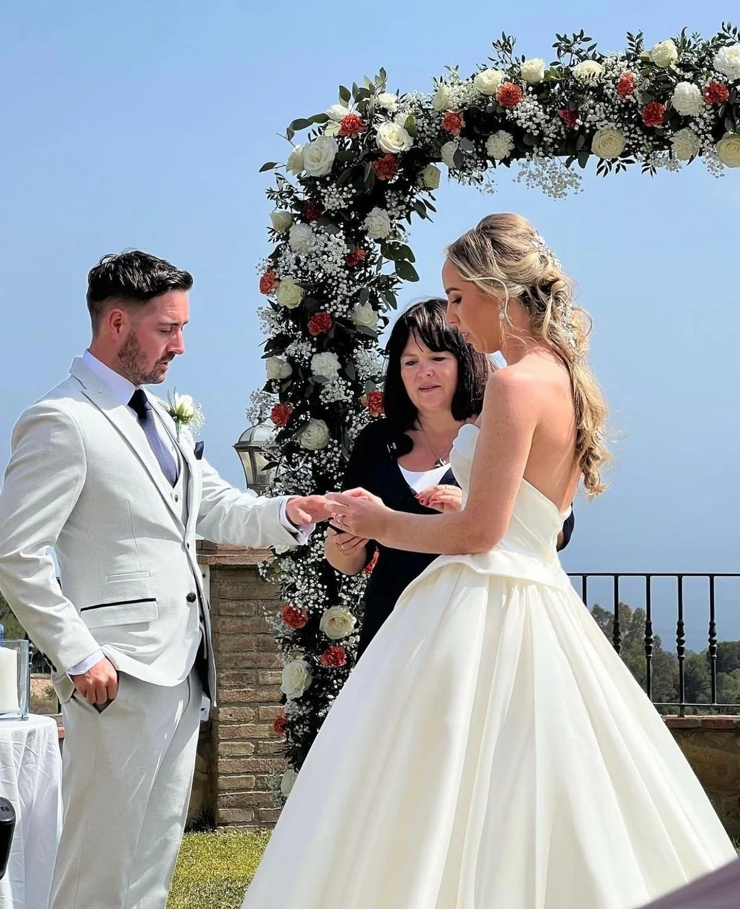A couple getting married outdoors under a floral arch with officiant overseeing the ceremony.