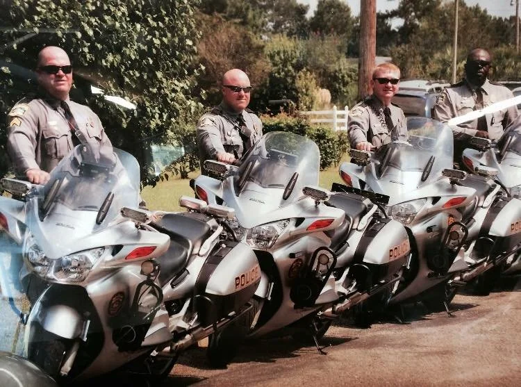 An aged picture of four police officers, one of them Chris Stephens, standing next to their police motorcycles outdoors.