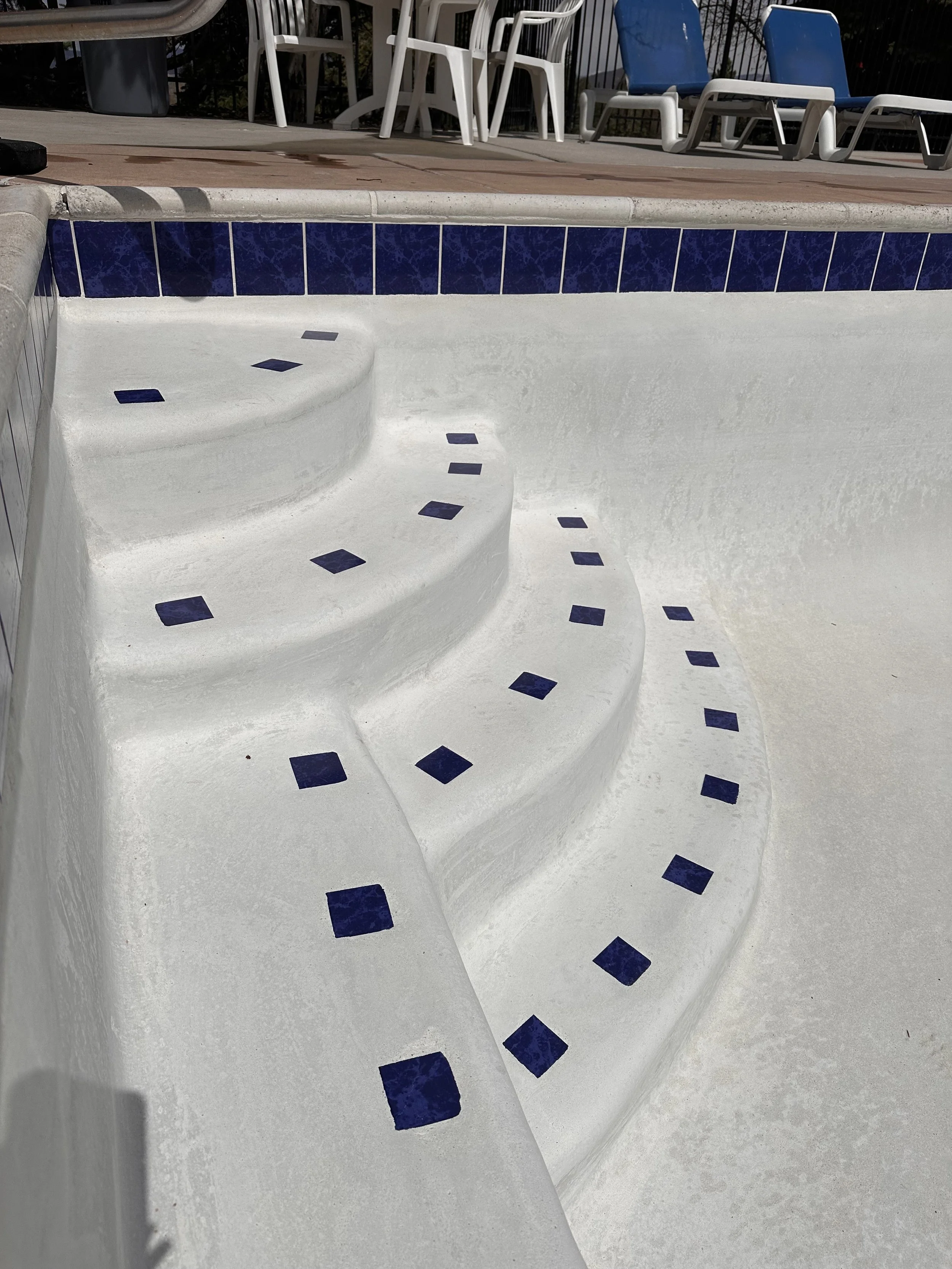 After picture of empty large pool with shiny white plaster and blue tiles.