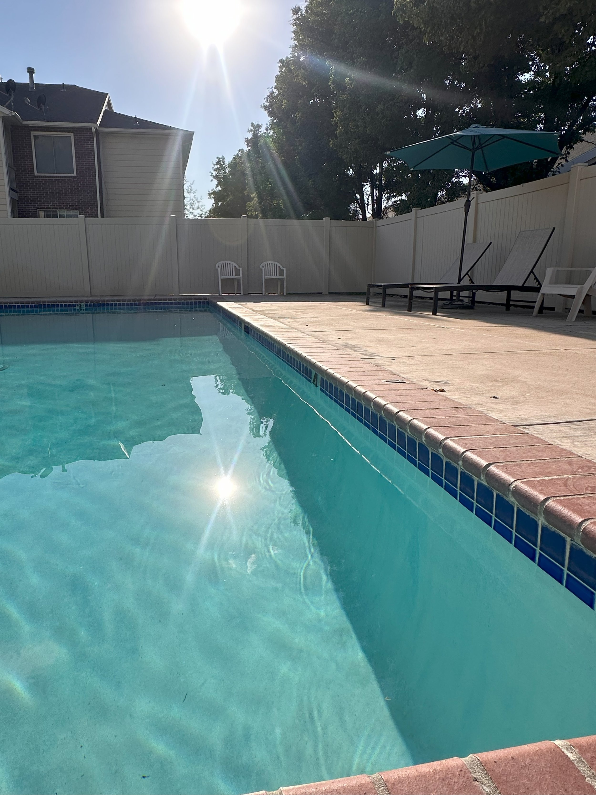Empty swimming pool with clear blue water, neatly placed pool deck furniture is seen in the background. 