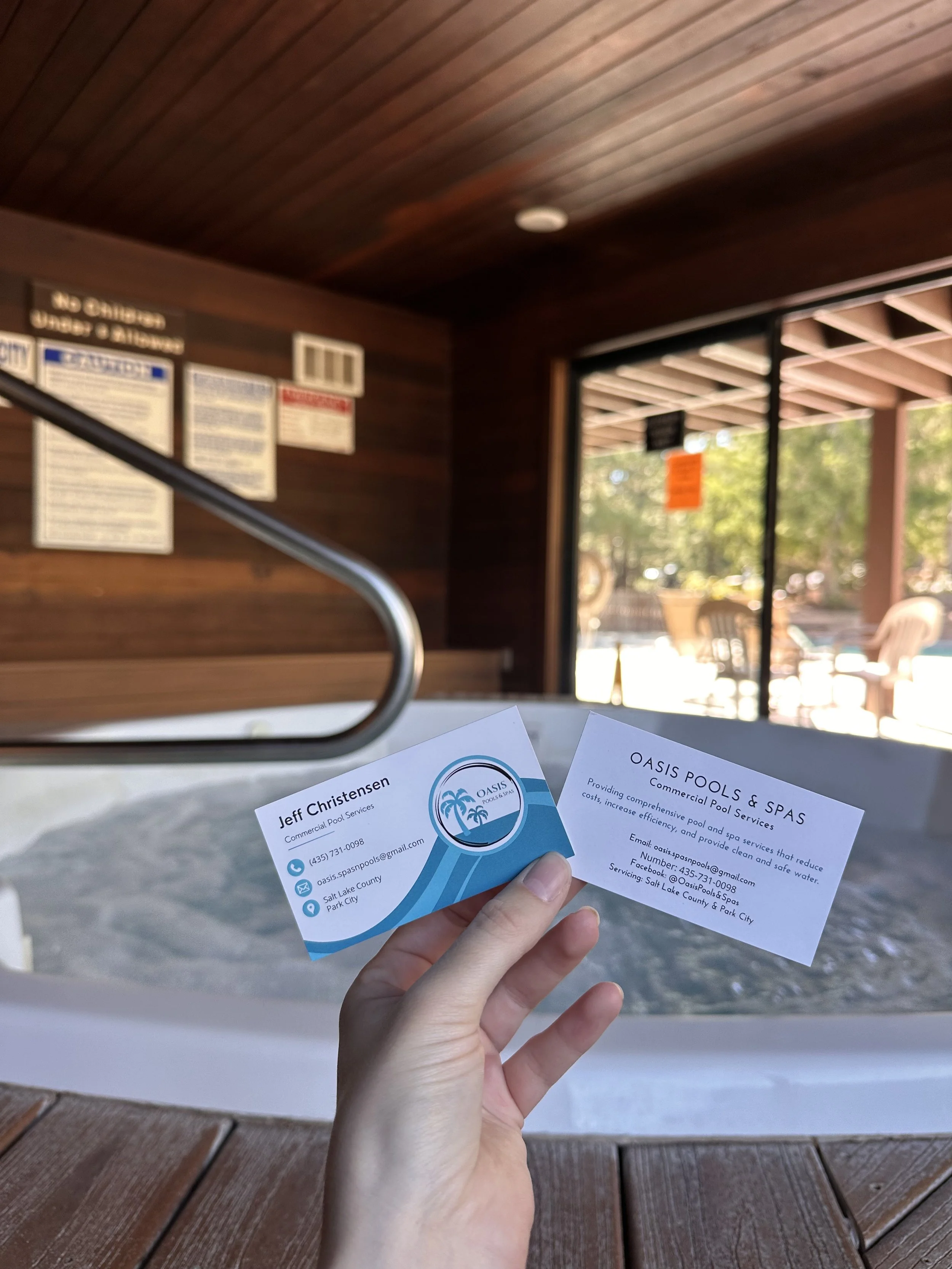 Womans hand holding two business cards, a small hot tub is visible in the background.