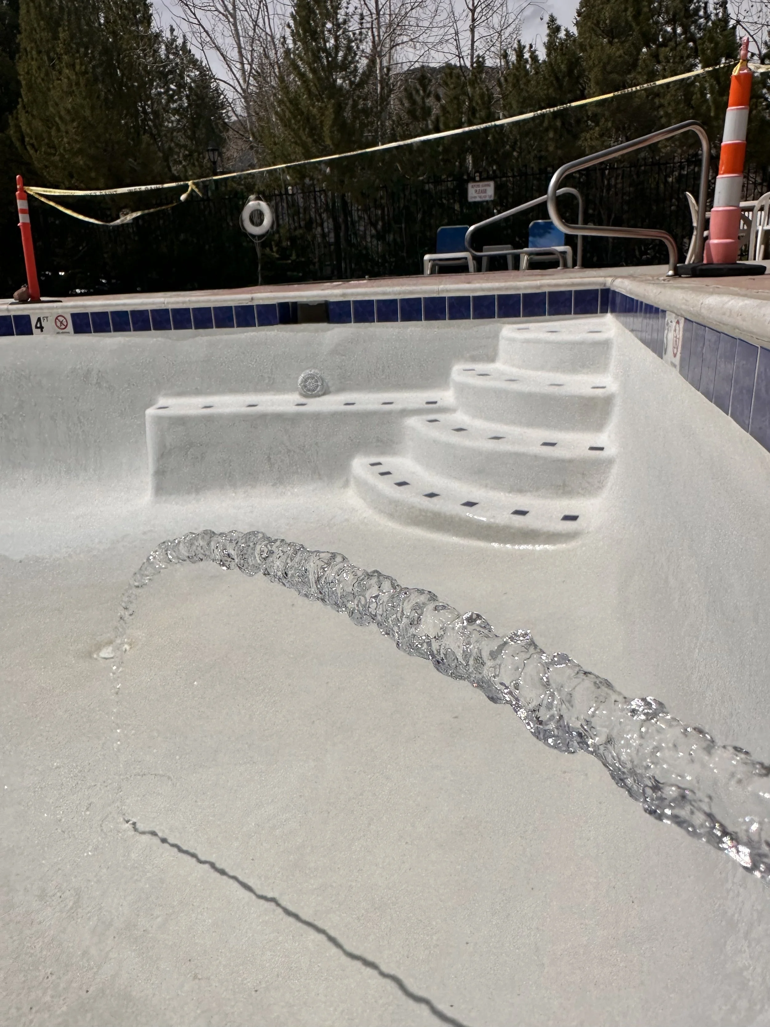 A swimming pool with no water, shiny white plaster, and clean blue tiles. A hose is visible beginning to fill the empty pool. 
