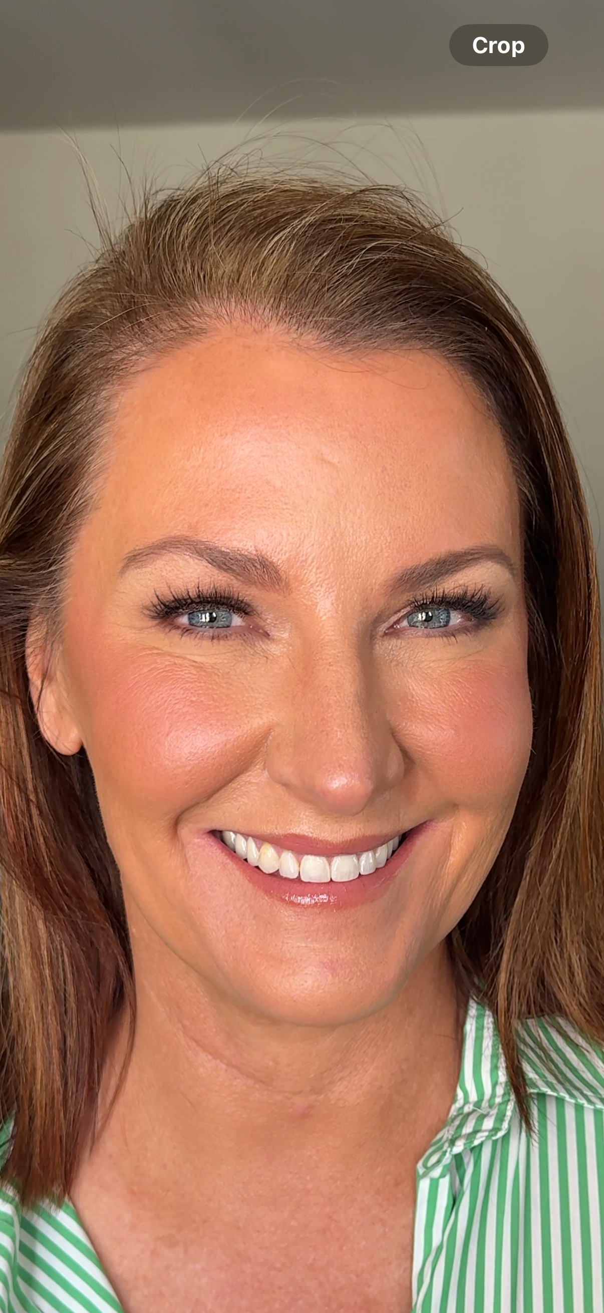 Close-up of a smiling woman with blue eyes and brown hair, wearing a green and white striped shirt.